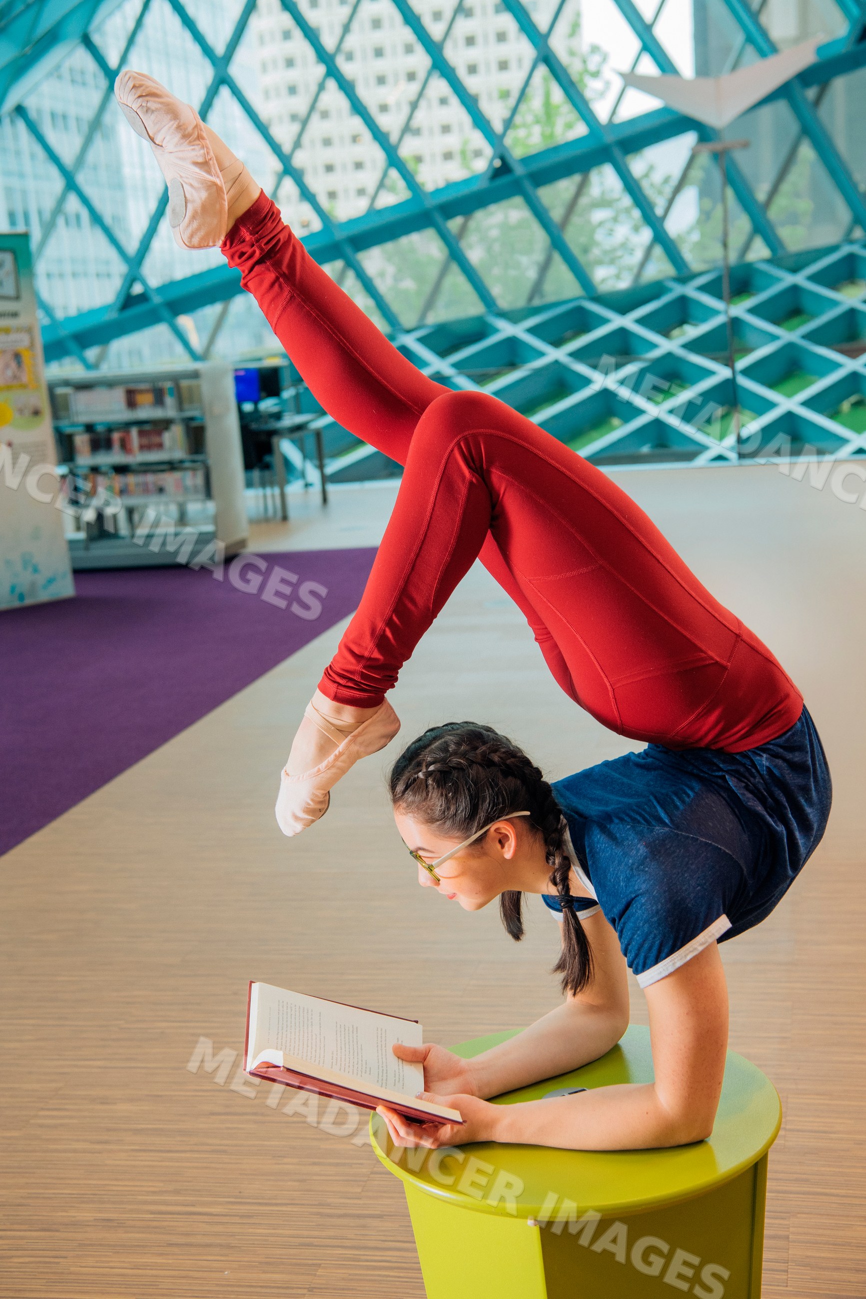 Young woman reads a book while doing a flexible yoga pose in a library