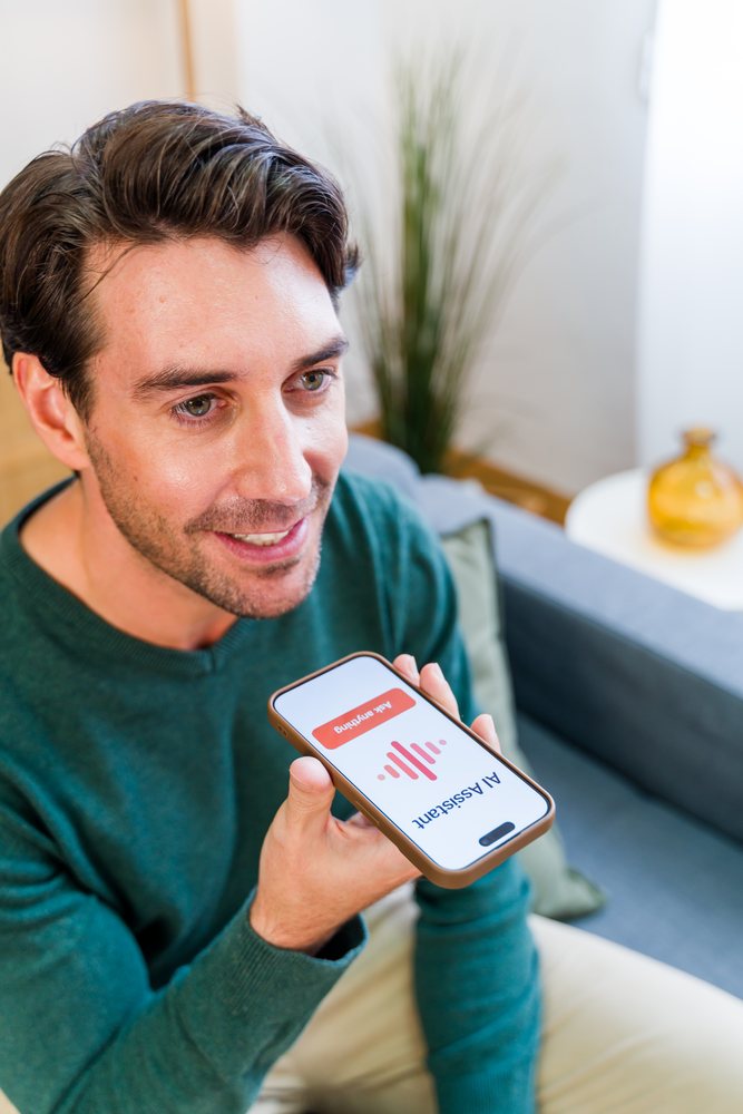 White man using smartphone voice assistant sitting on couch inside