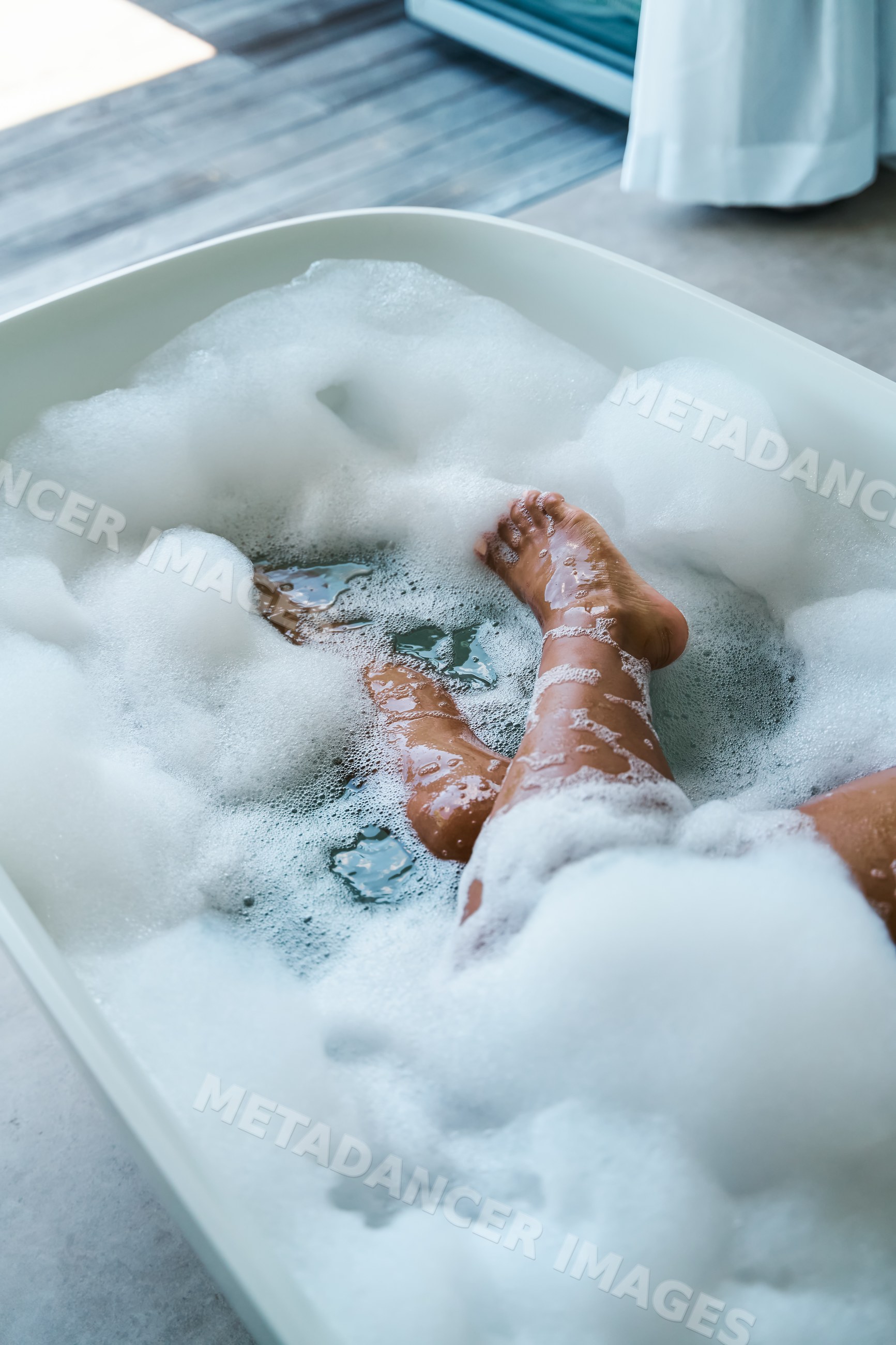 A white person relaxing in a bubble bath soaking legs and feet indoors