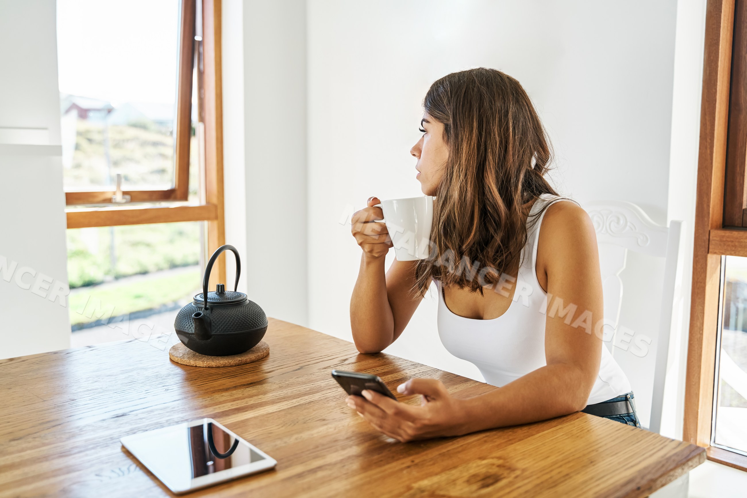 A white woman enjoys coffee and checks her phone by a wooden table