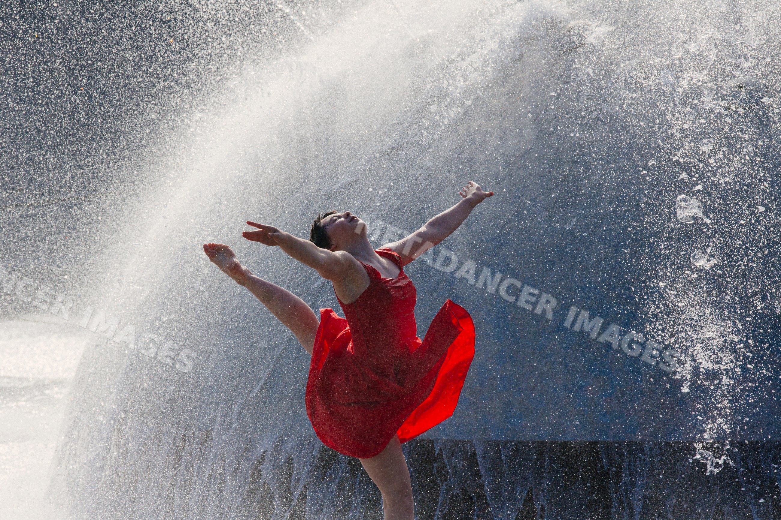White dancer leaping through water spray in red dress outdoors