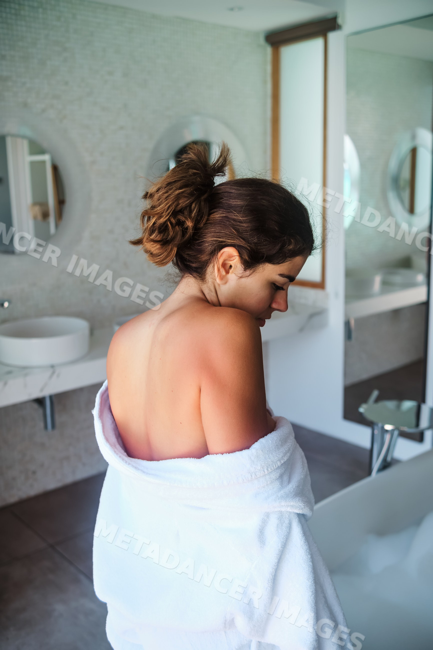 A white woman wrapped in a towel stands in a modern bathroom