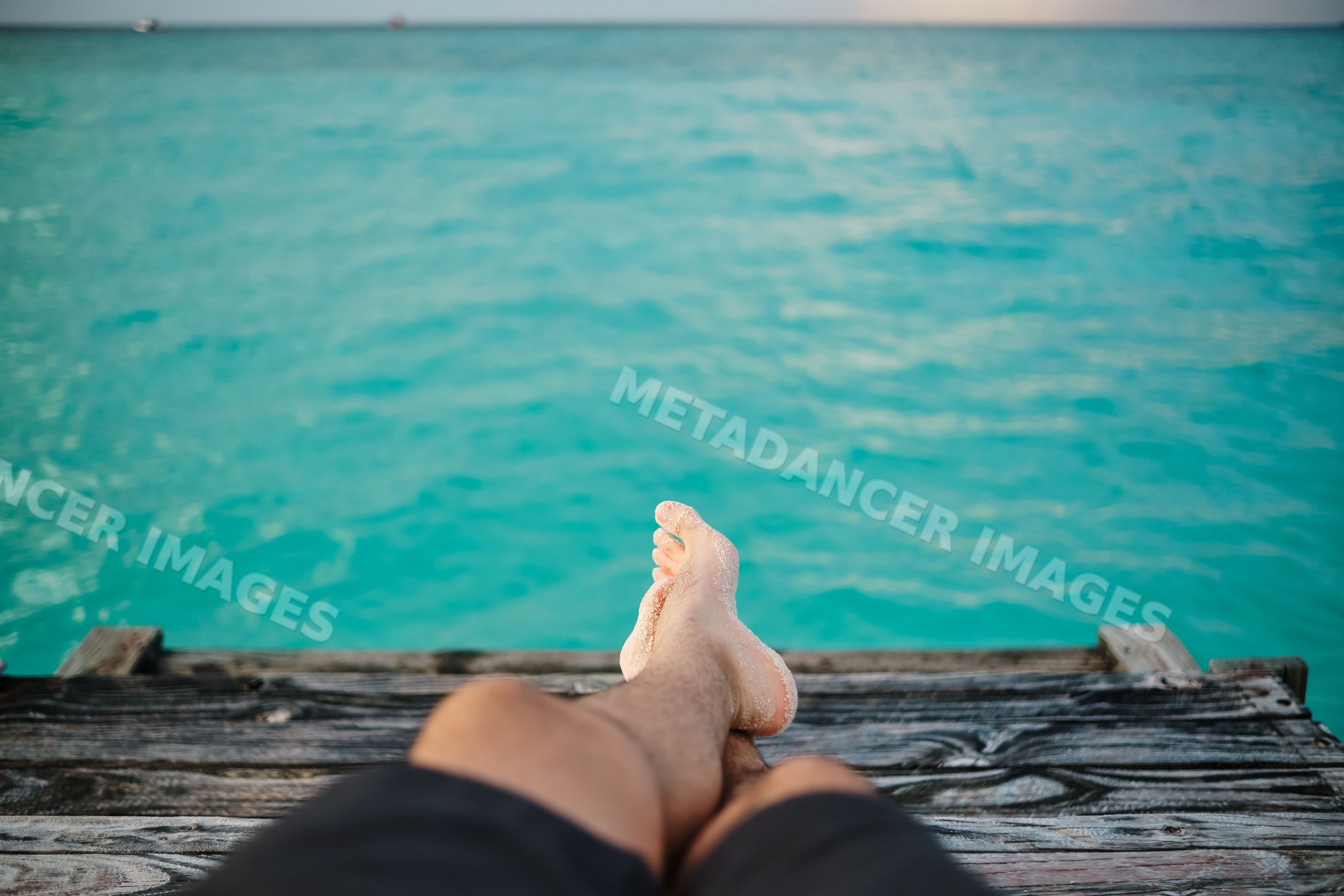 A person relaxing on a wooden pier overlooking turquoise water