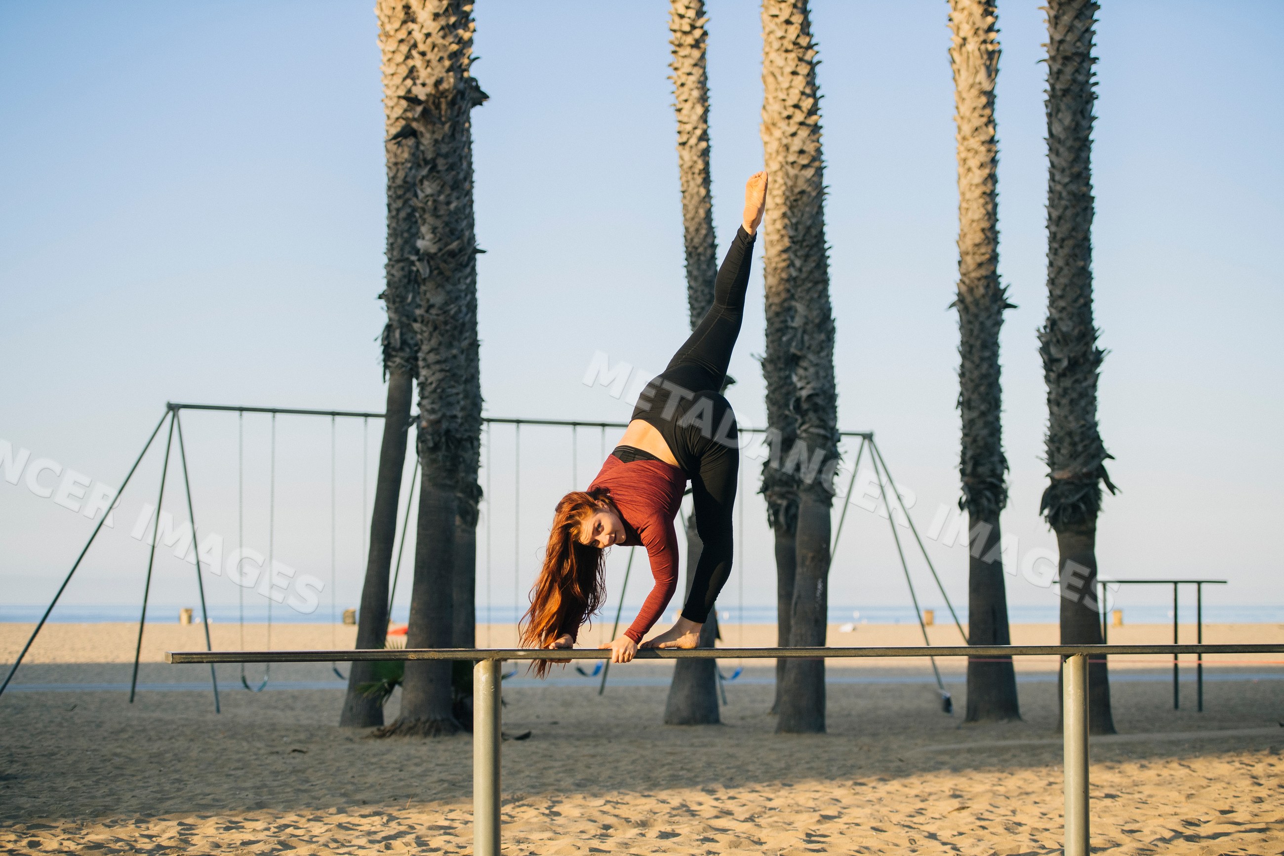 White woman exercising on balance beam at beach with palm trees