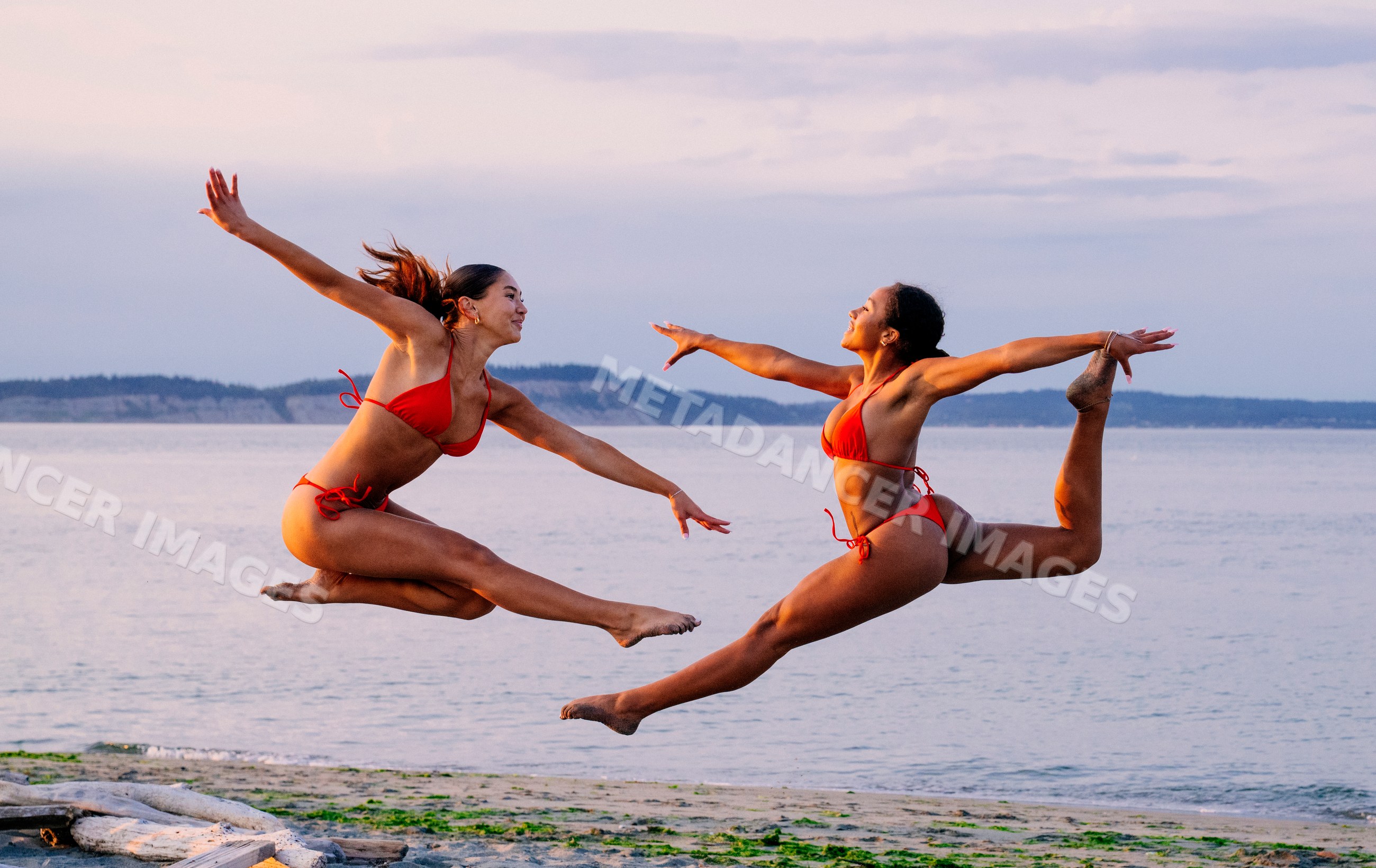 Two women perform acrobatic jumps on a beach at twilight in WA, USA