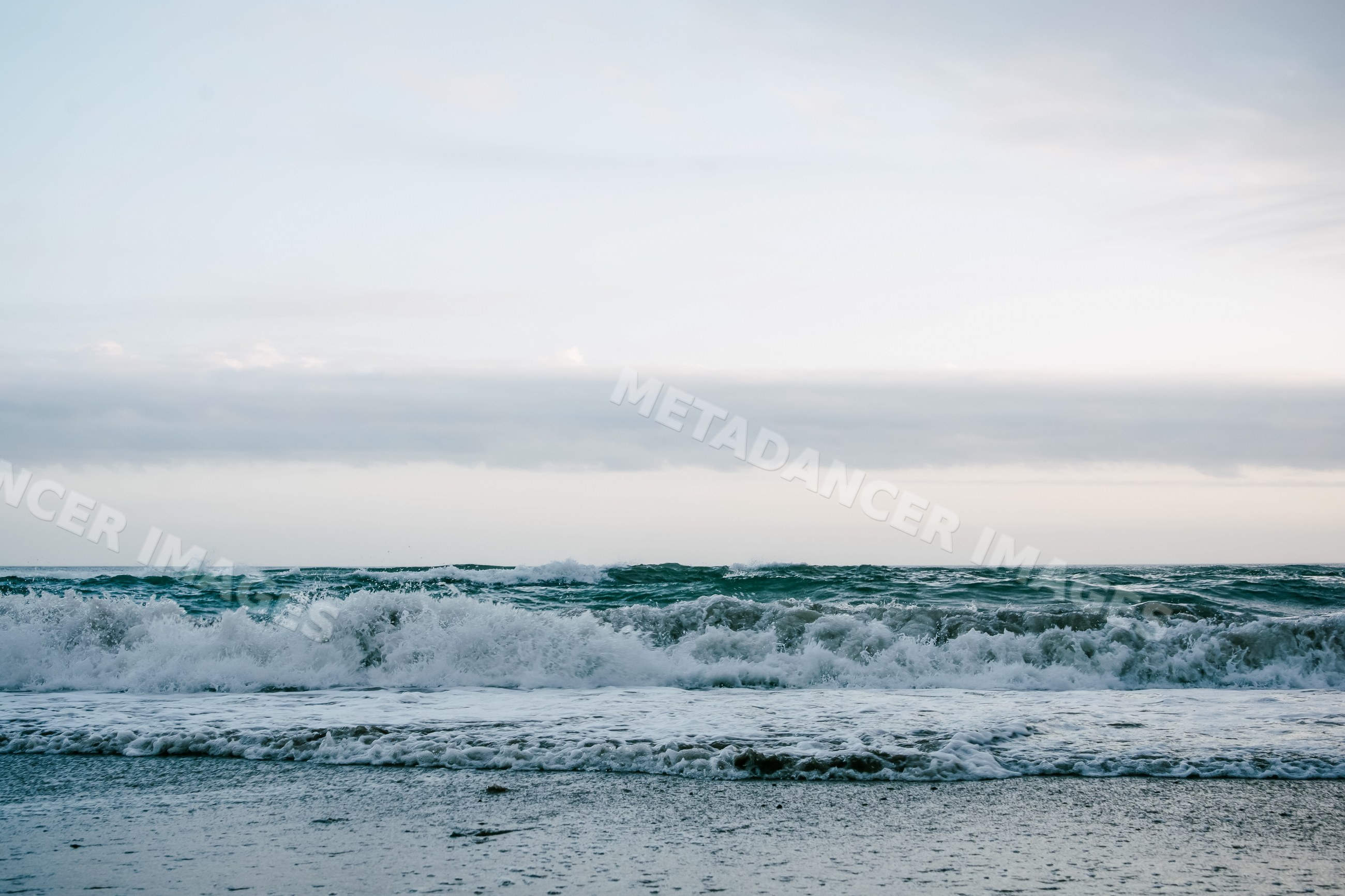 Ocean waves breaking with foam under cloudy sky at shore in Spain