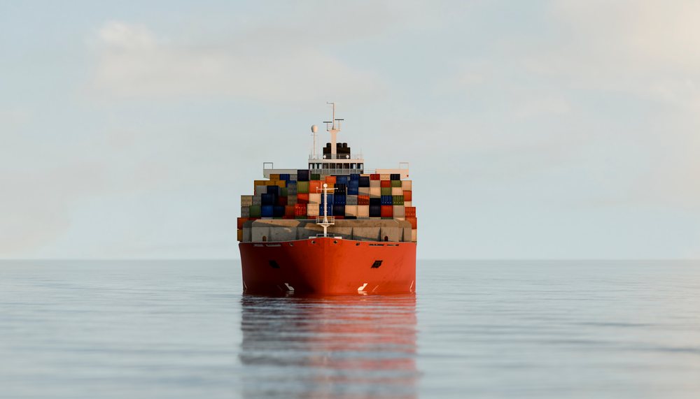 A red container ship loaded with cargo containers sails on calm ocean