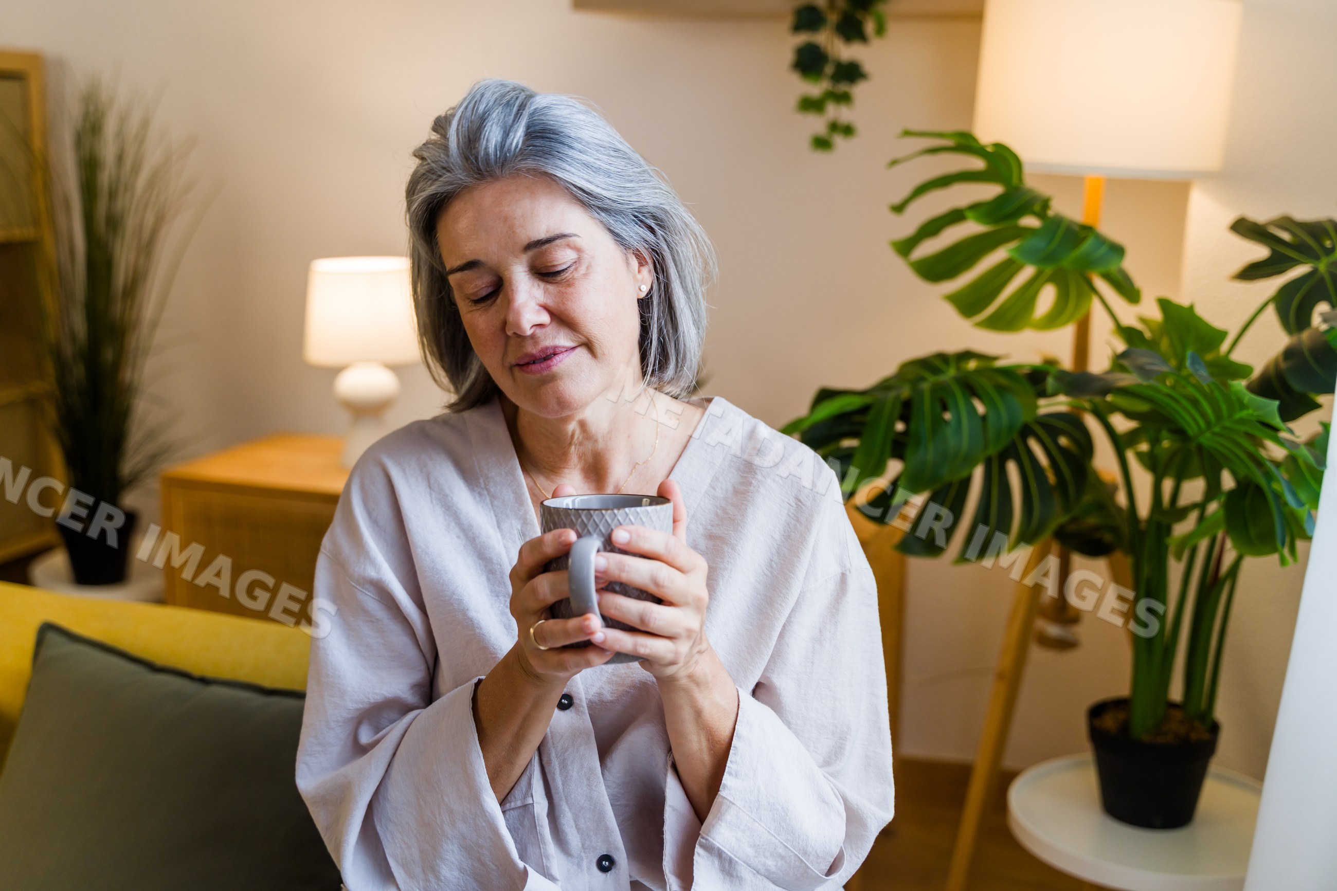 White woman holding cup and relaxing on sofa in cozy home in Spain