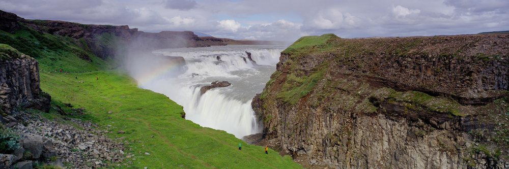 Waterfall with rainbow over rocky cliffs and green landscape