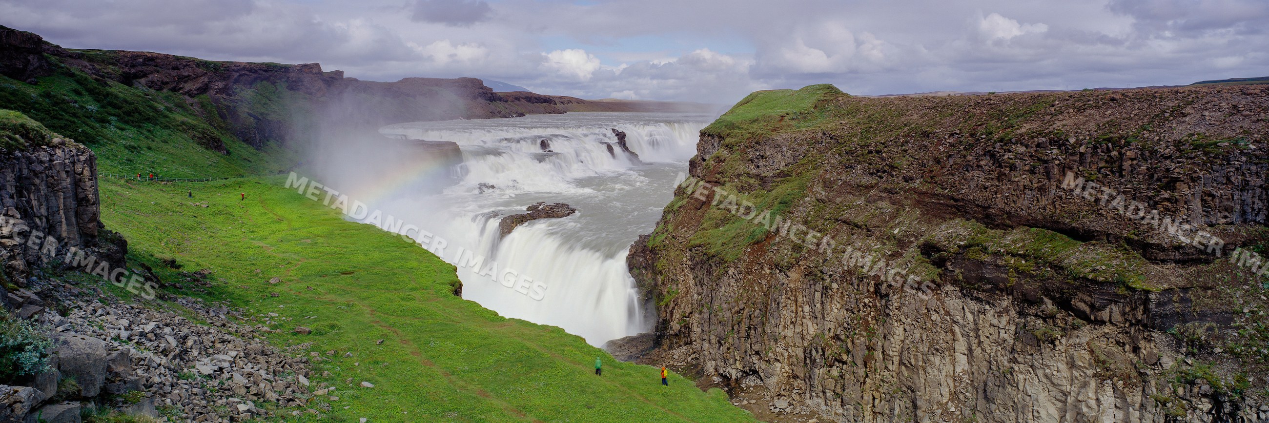 Waterfall with rainbow over rocky cliffs and green landscape