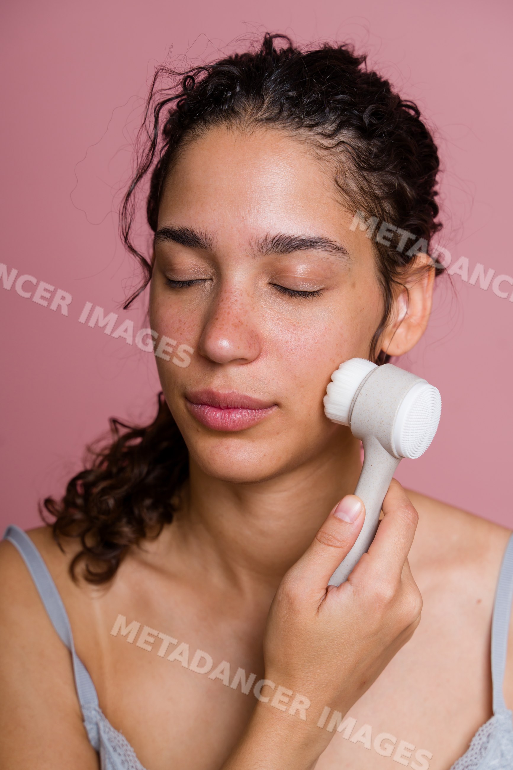 Hispanic woman using facial cleansing brush