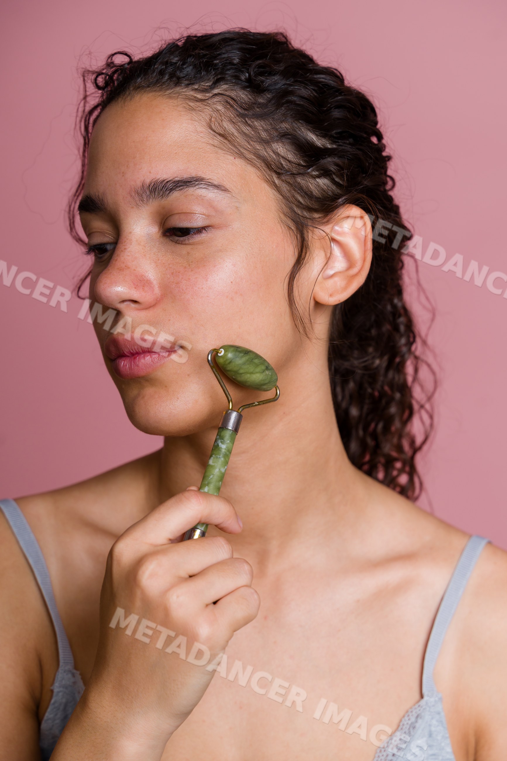 Hispanic woman using jade roller for facial massage in beauty shoot