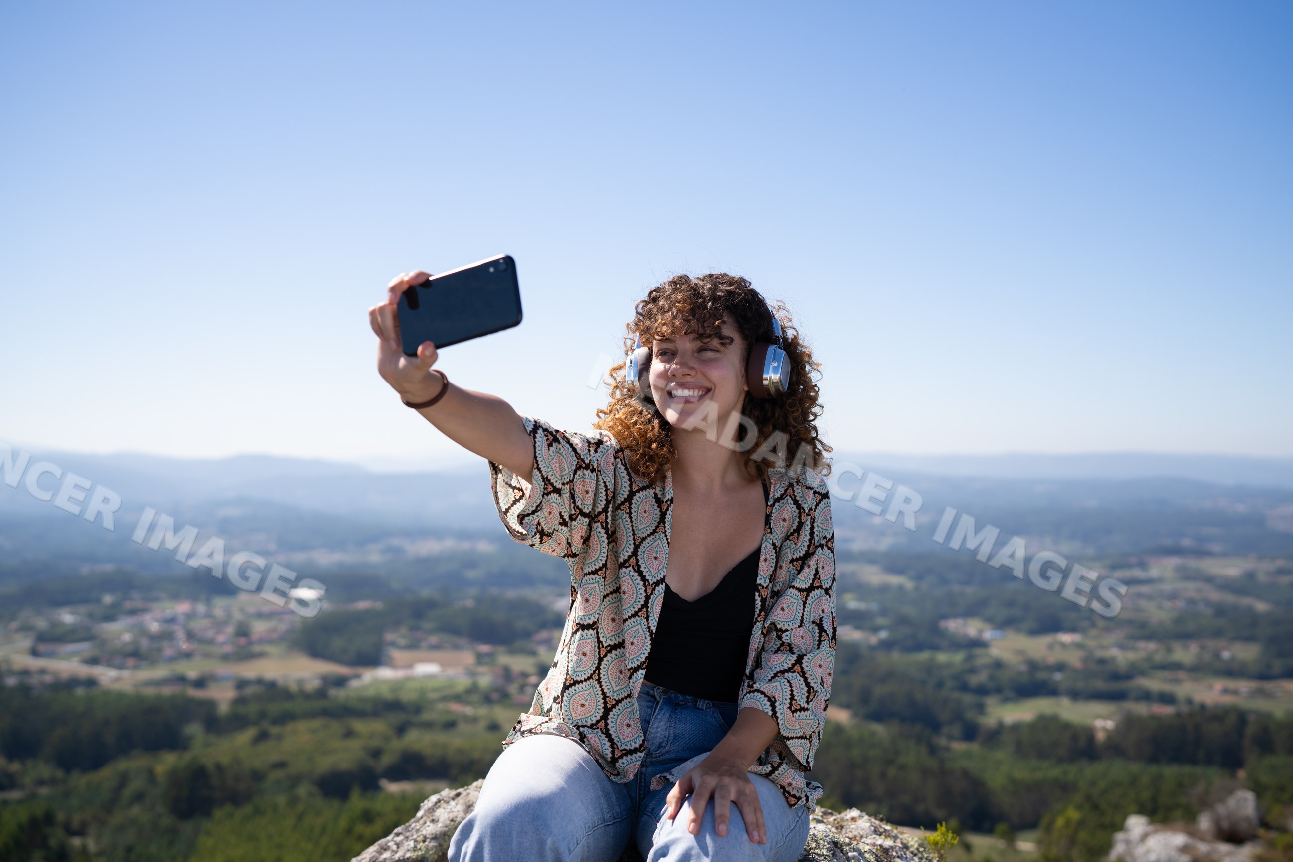 White woman taking selfie with smartphone on hilltop overlooking