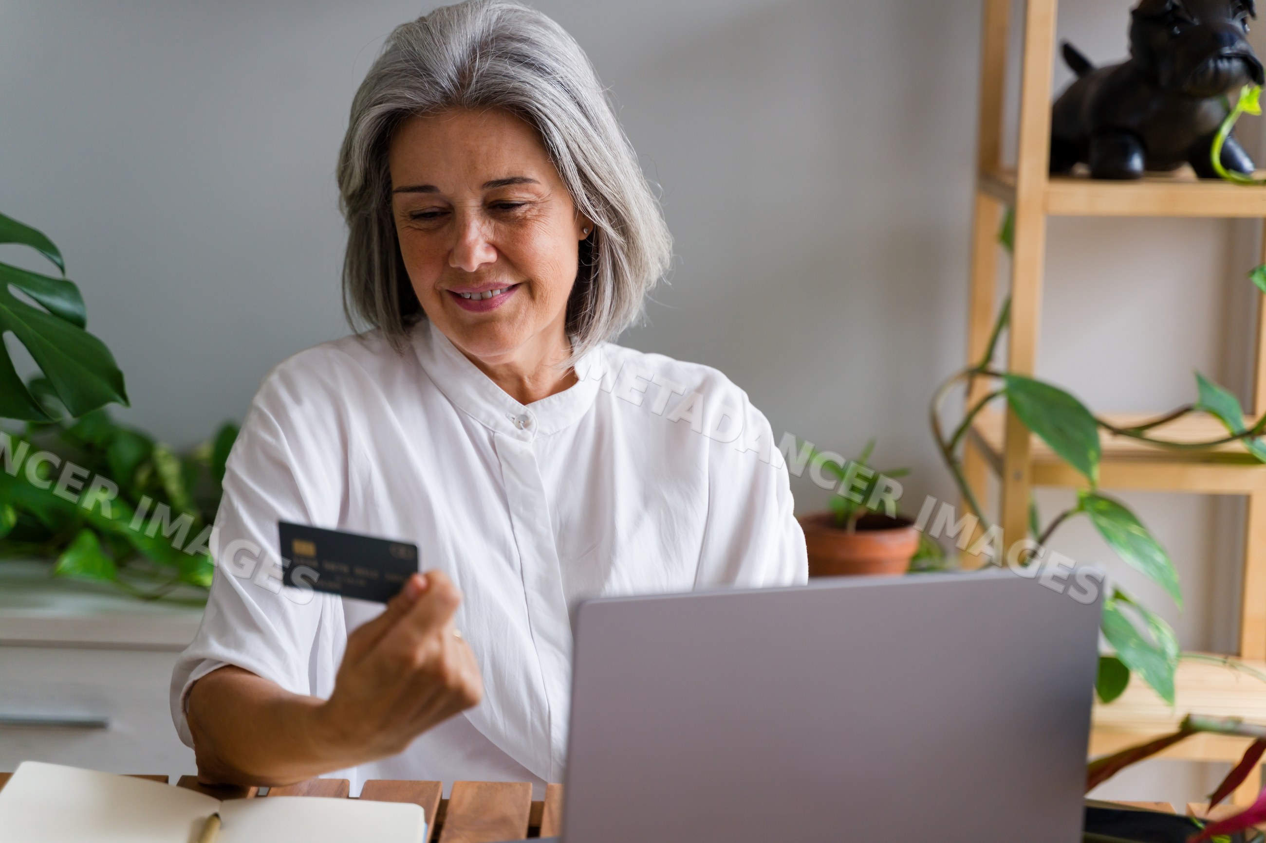 Mature white woman using laptop and payment card for online shopping