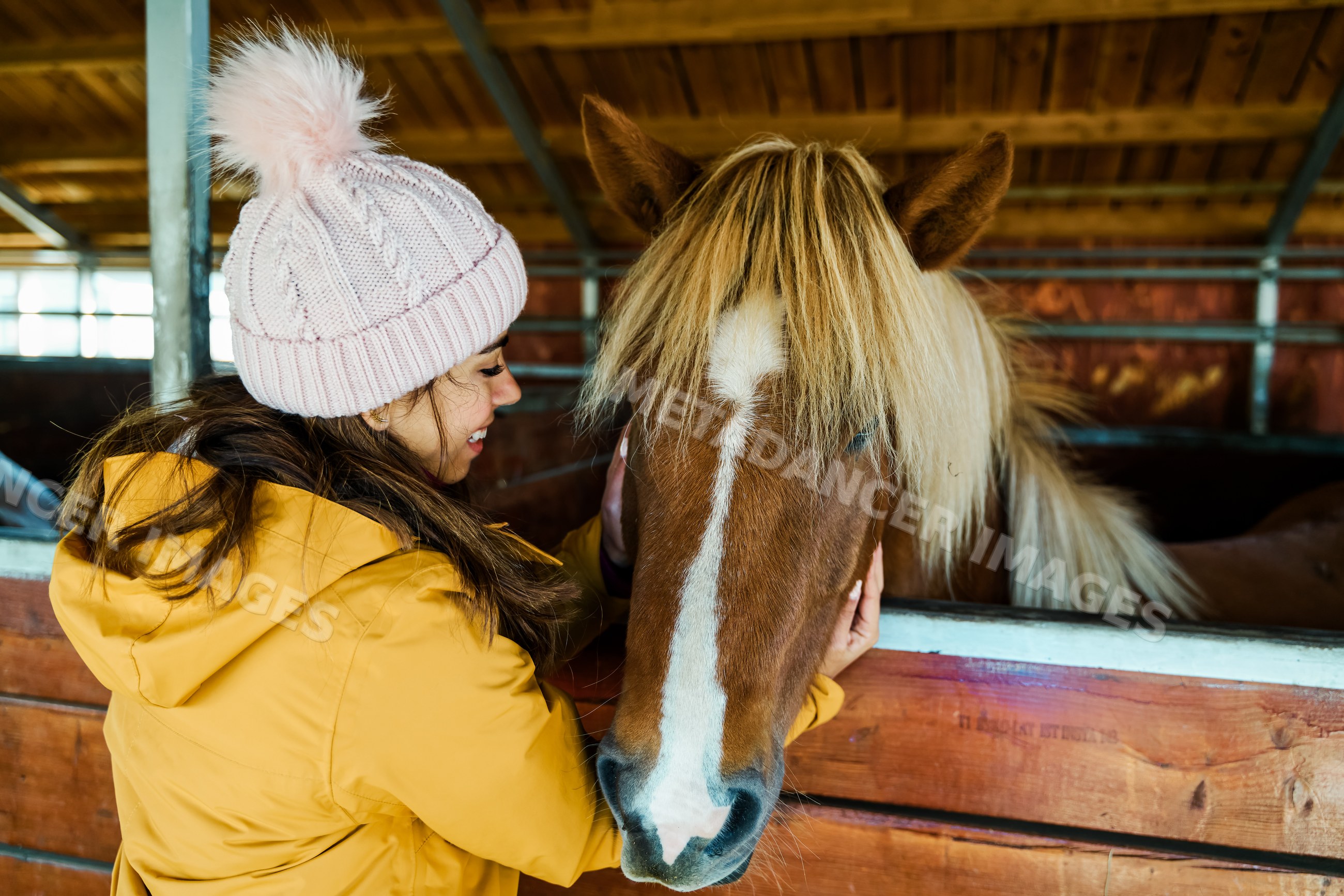 A white woman gently pets a brown horse inside a wooden stable