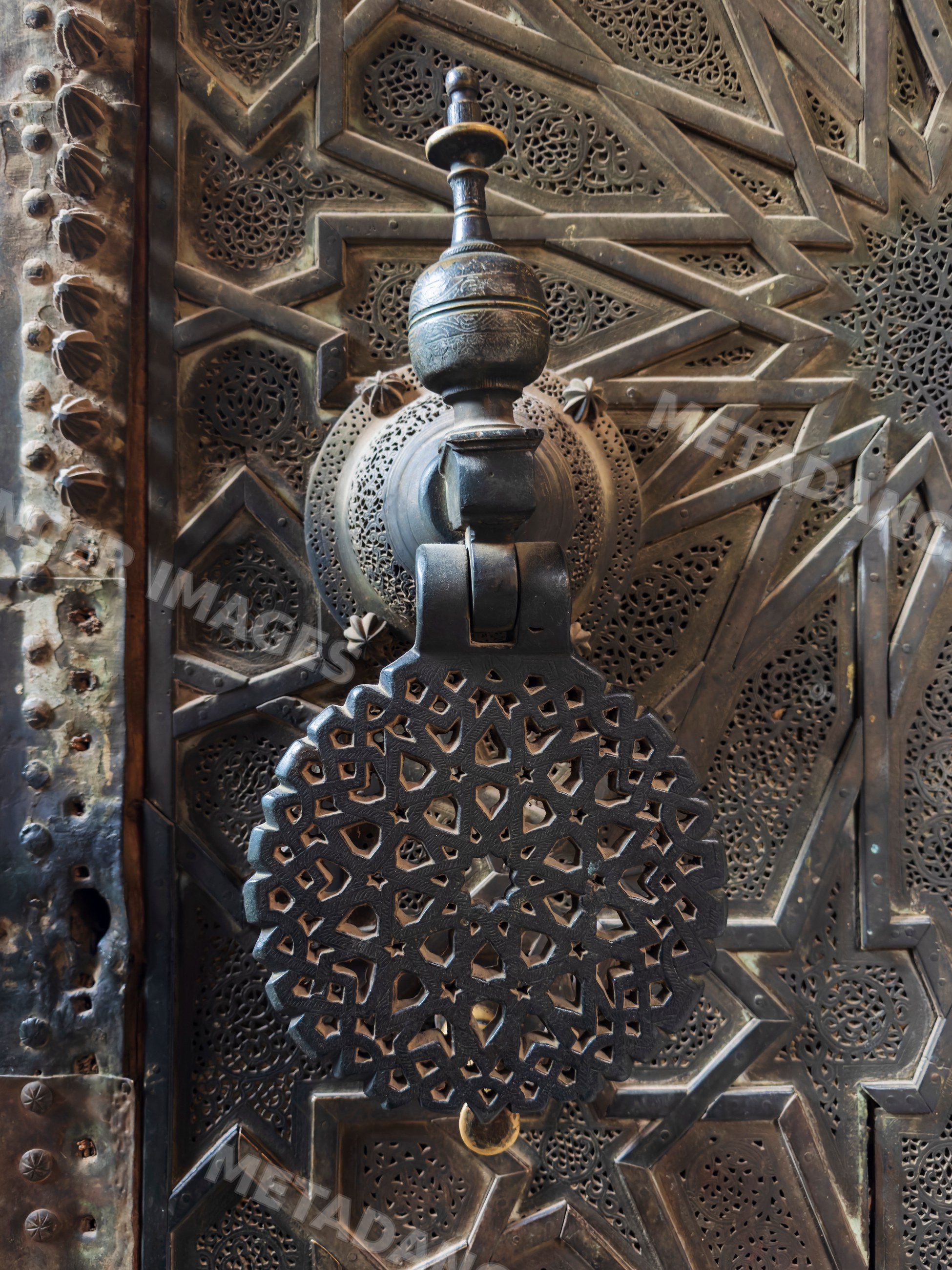 Ornate metal door knocker with intricate geometric patterns at medresa