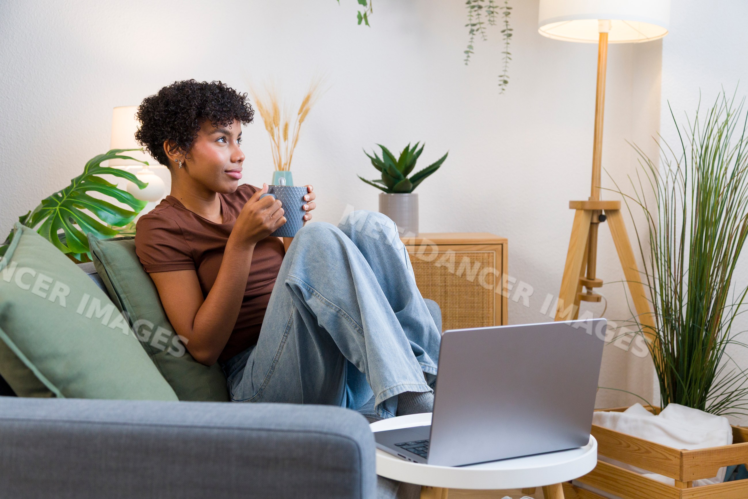 Young African American woman holding mug on sofa with laptop