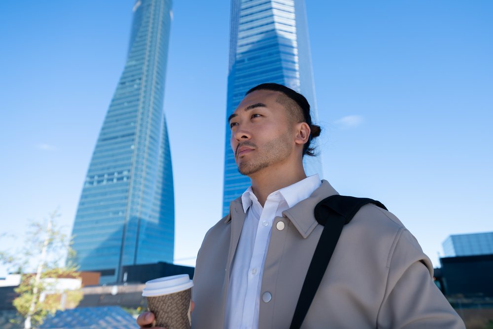 Man holding coffee cup outdoors with modern skyscrapers in Madrid
