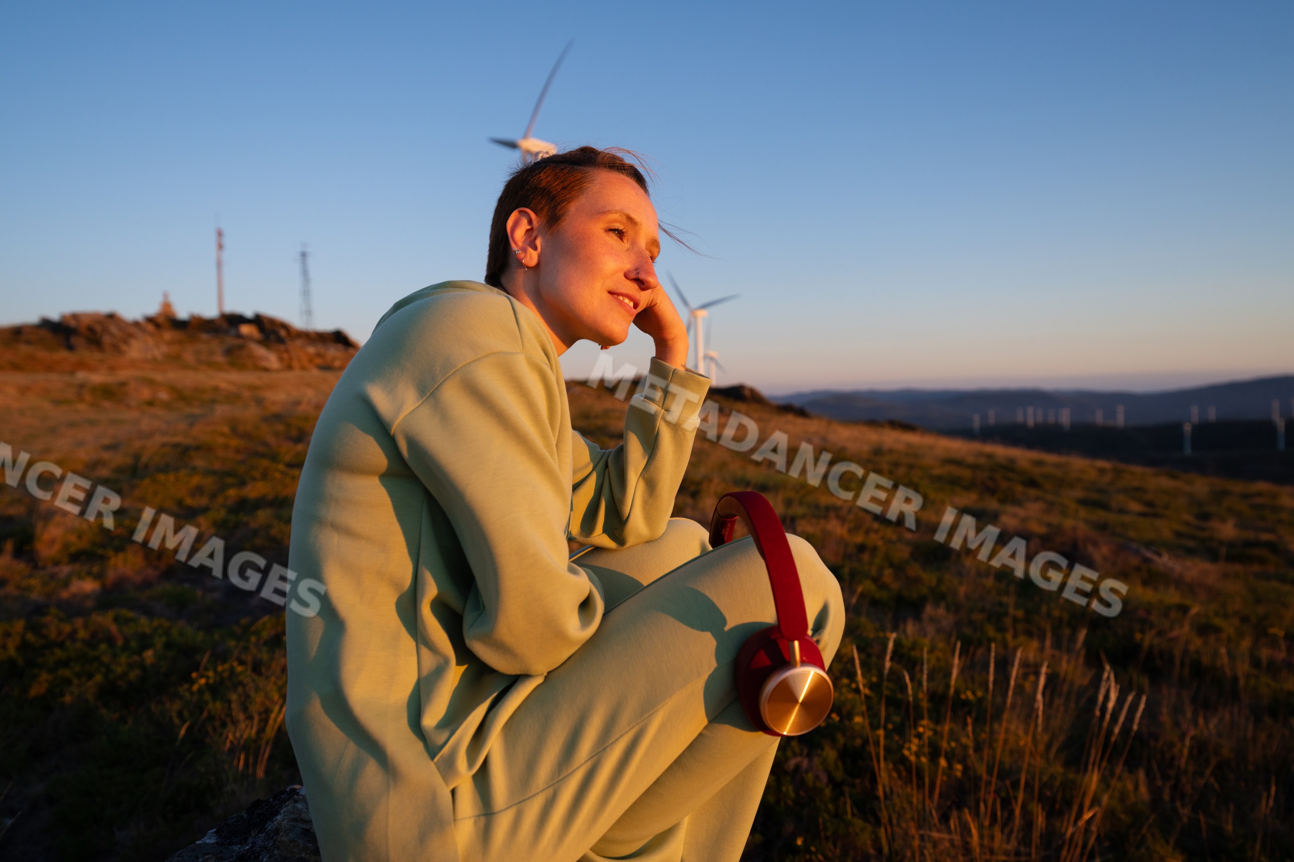 A white woman enjoys a peaceful sunset with wind turbines in Galicia