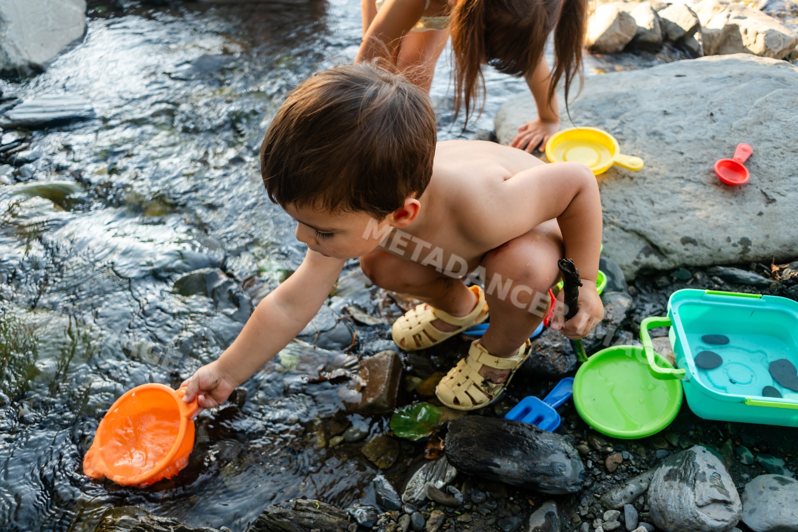 Young white boy playing with water toys on a rocky riverbank
