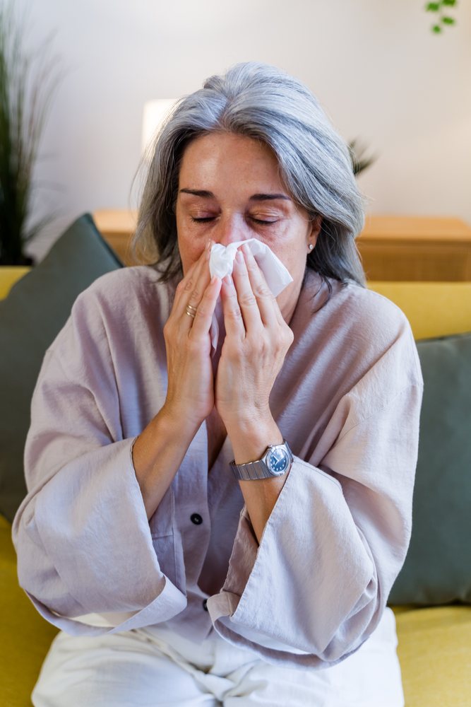 White woman blowing nose with tissue on couch indoors