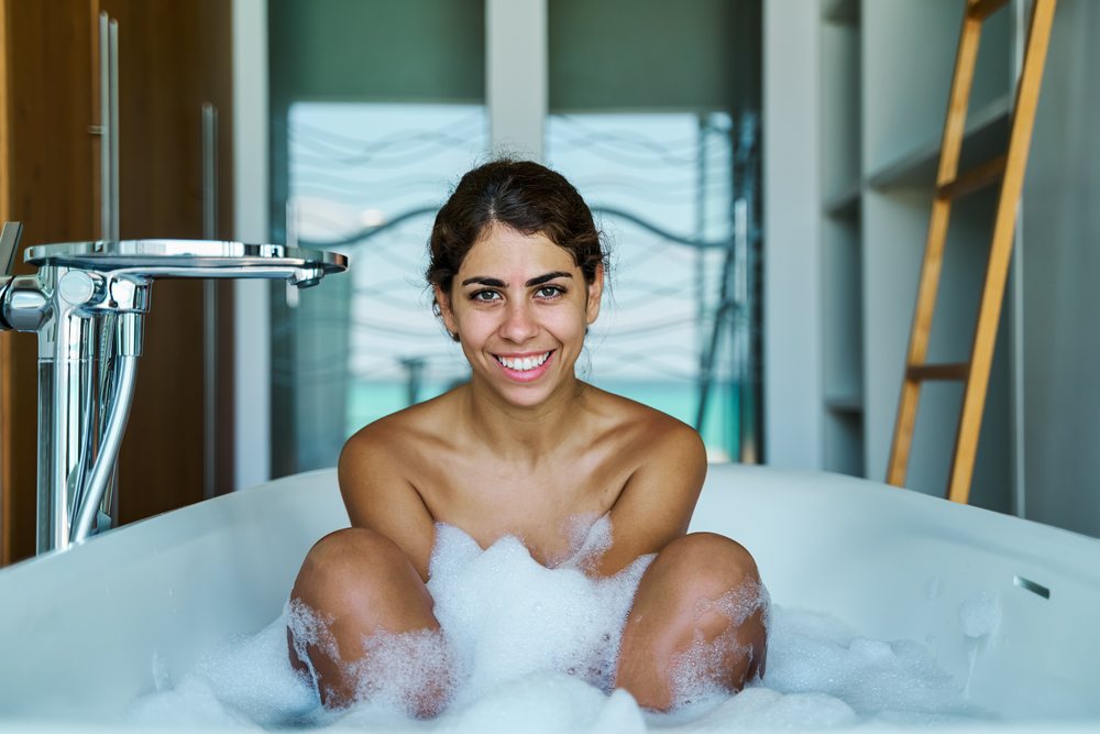 A white woman enjoying a relaxing bubble bath in a modern bathroom