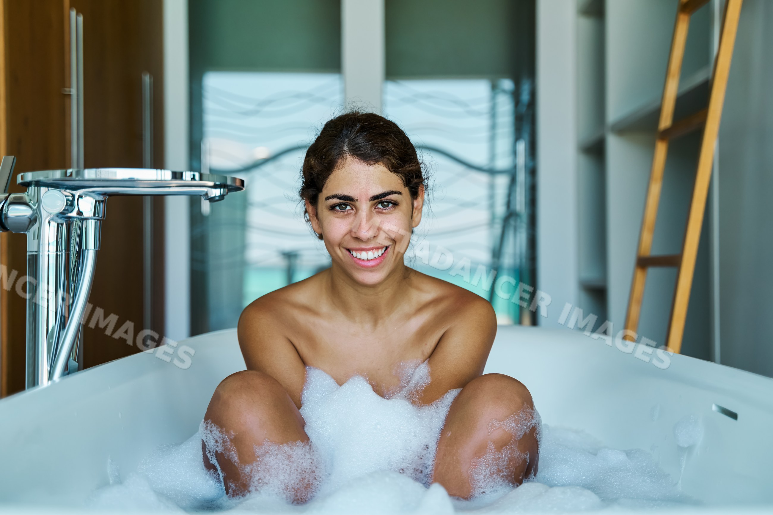 A white woman enjoying a relaxing bubble bath in a modern bathroom