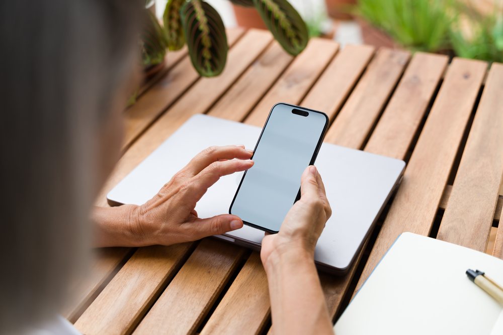 Smartphone held over closed laptop on wooden table