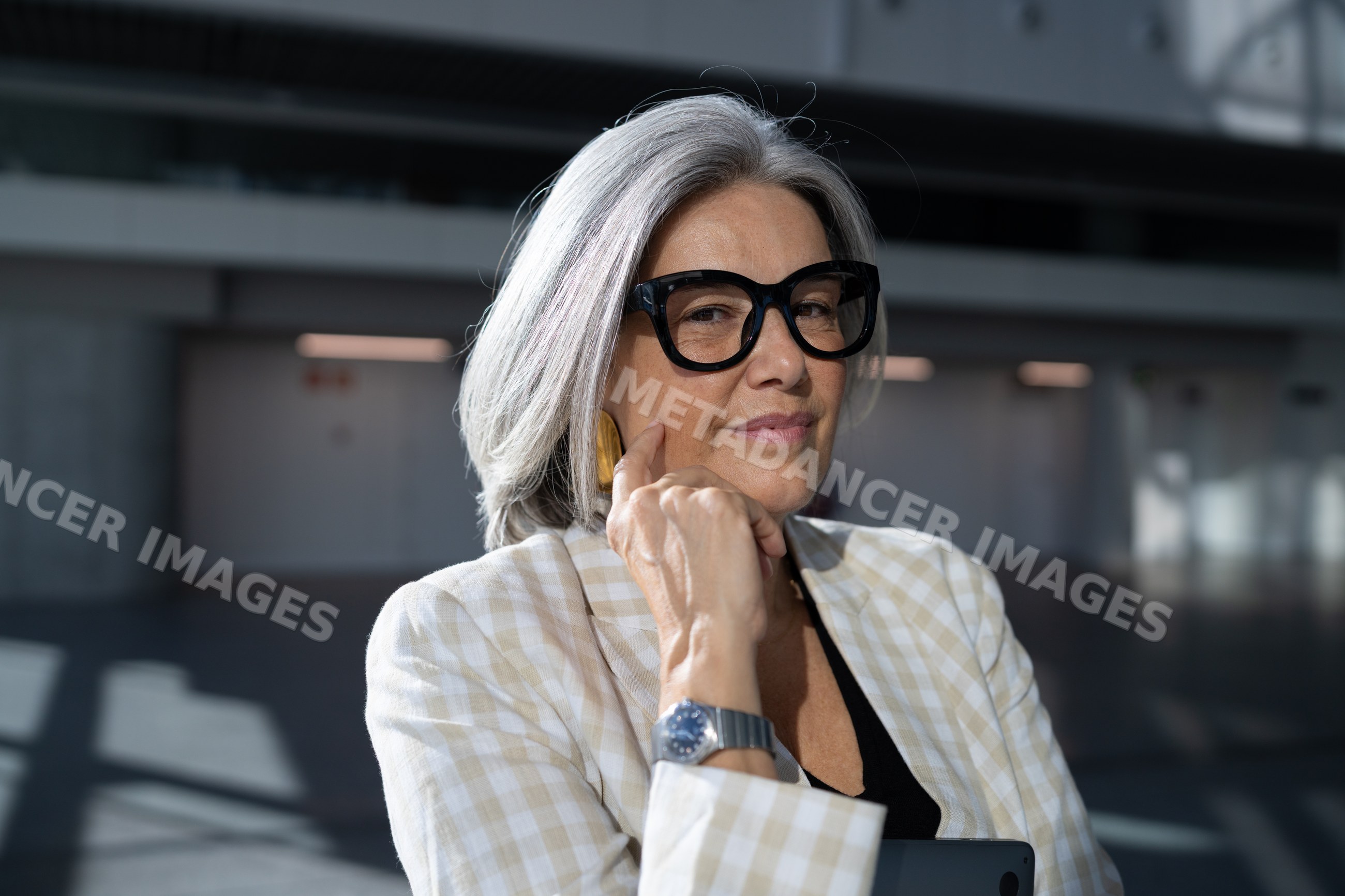 Mature white woman indoors wearing black glasses and plaid blazer