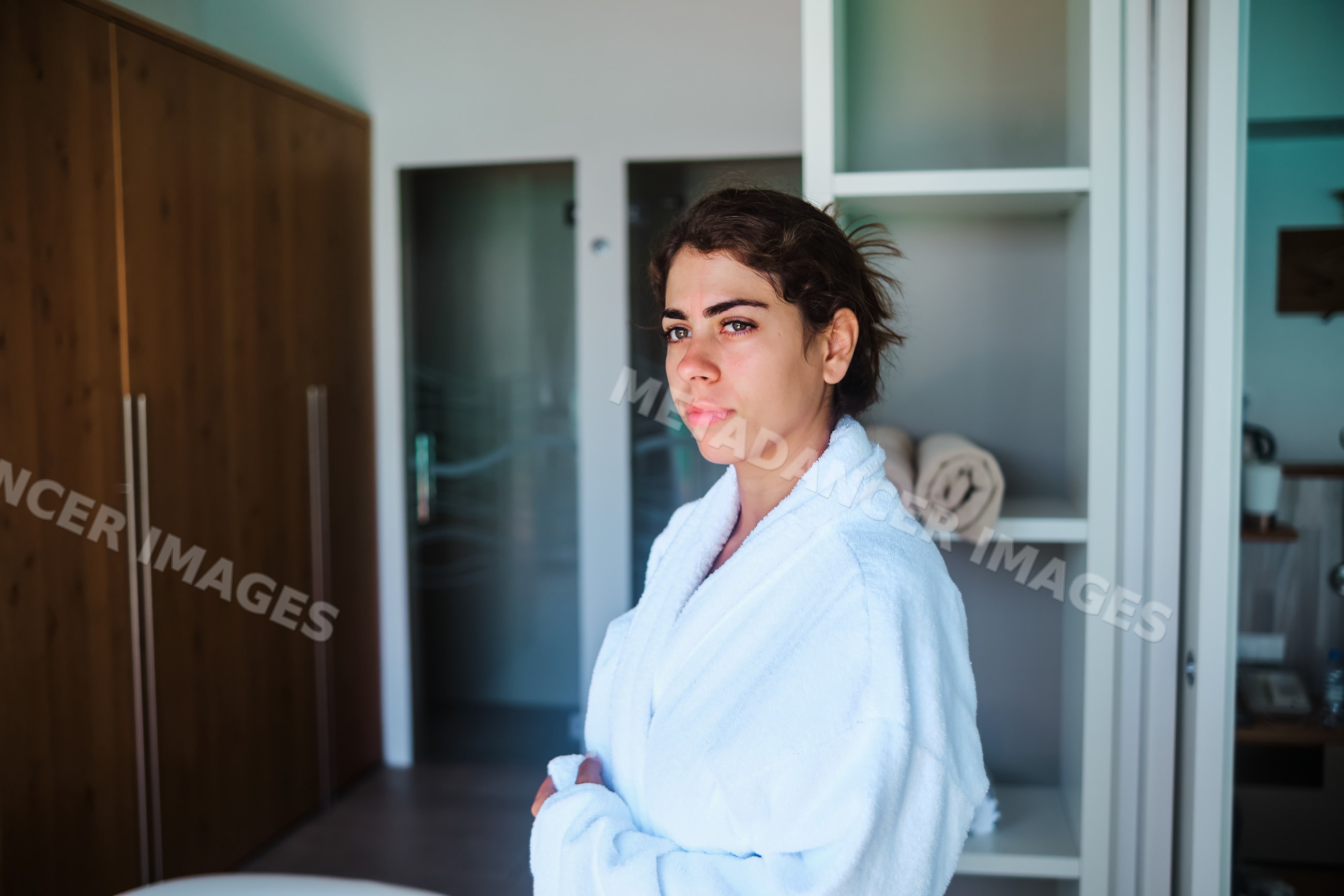 A woman in a white bathrobe stands contemplatively in a modern indoor