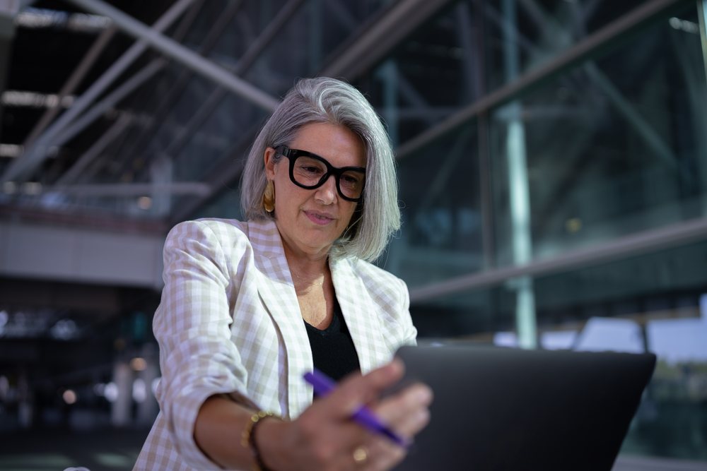 Businesswoman with gray hair uses tablet outside modern building