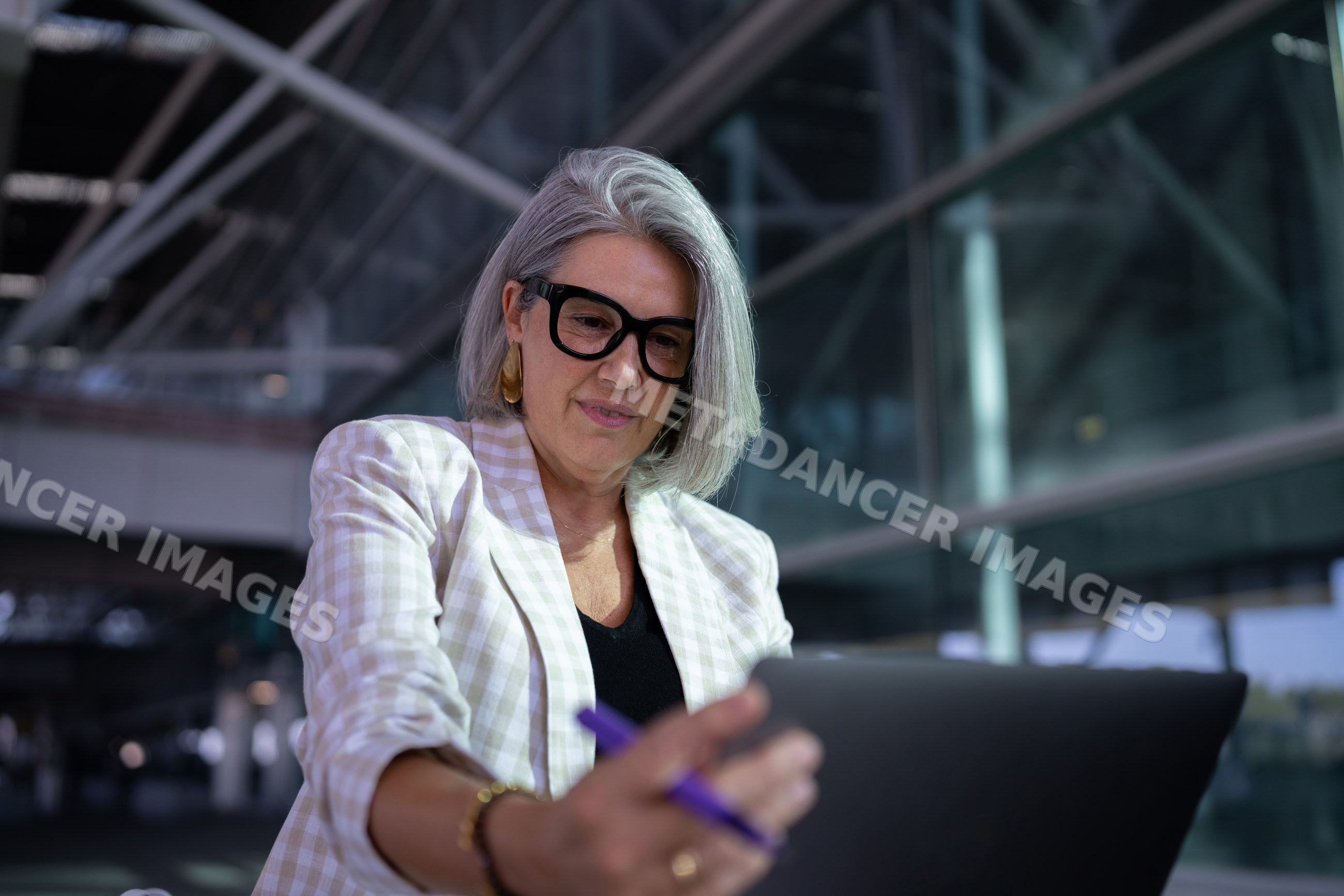 Businesswoman with gray hair uses tablet outside modern building