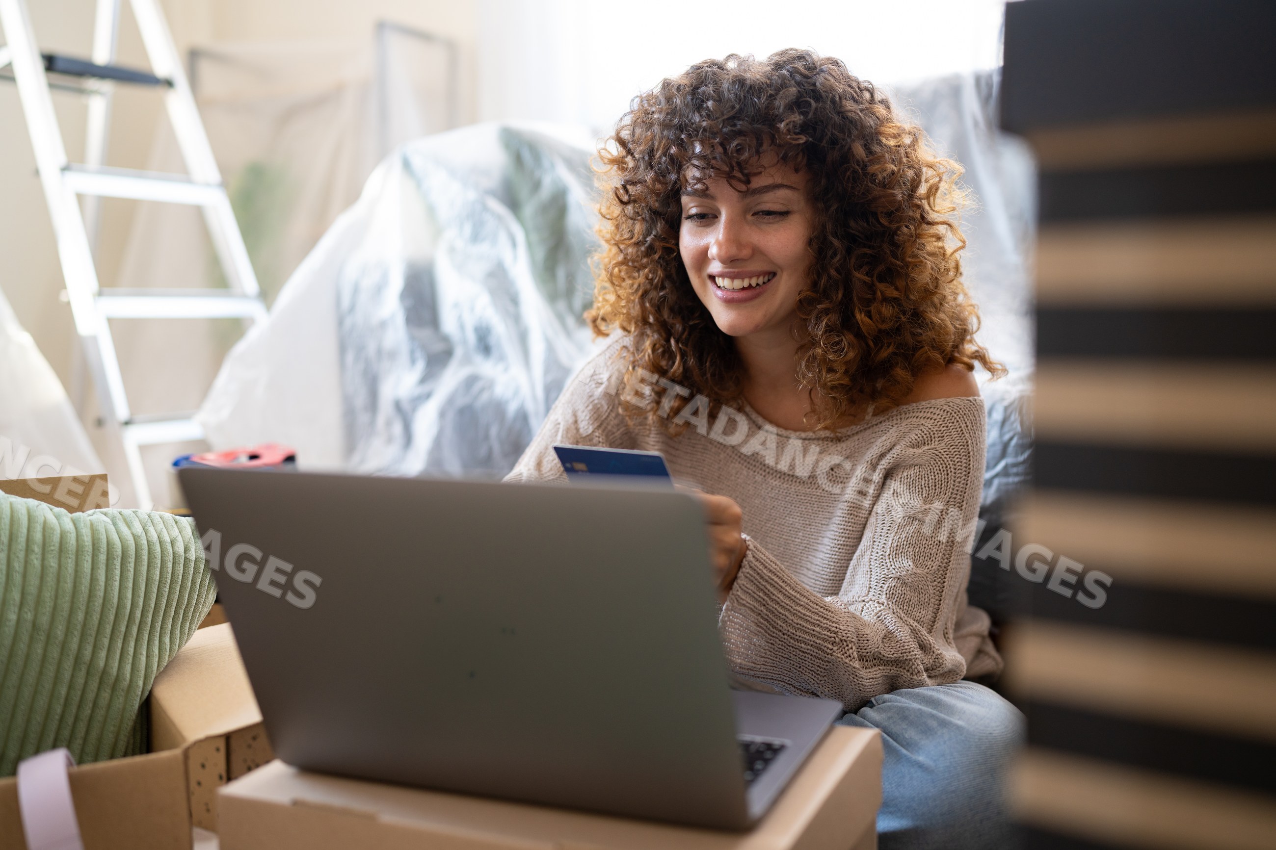 White woman using laptop and credit card among moving boxes indoors