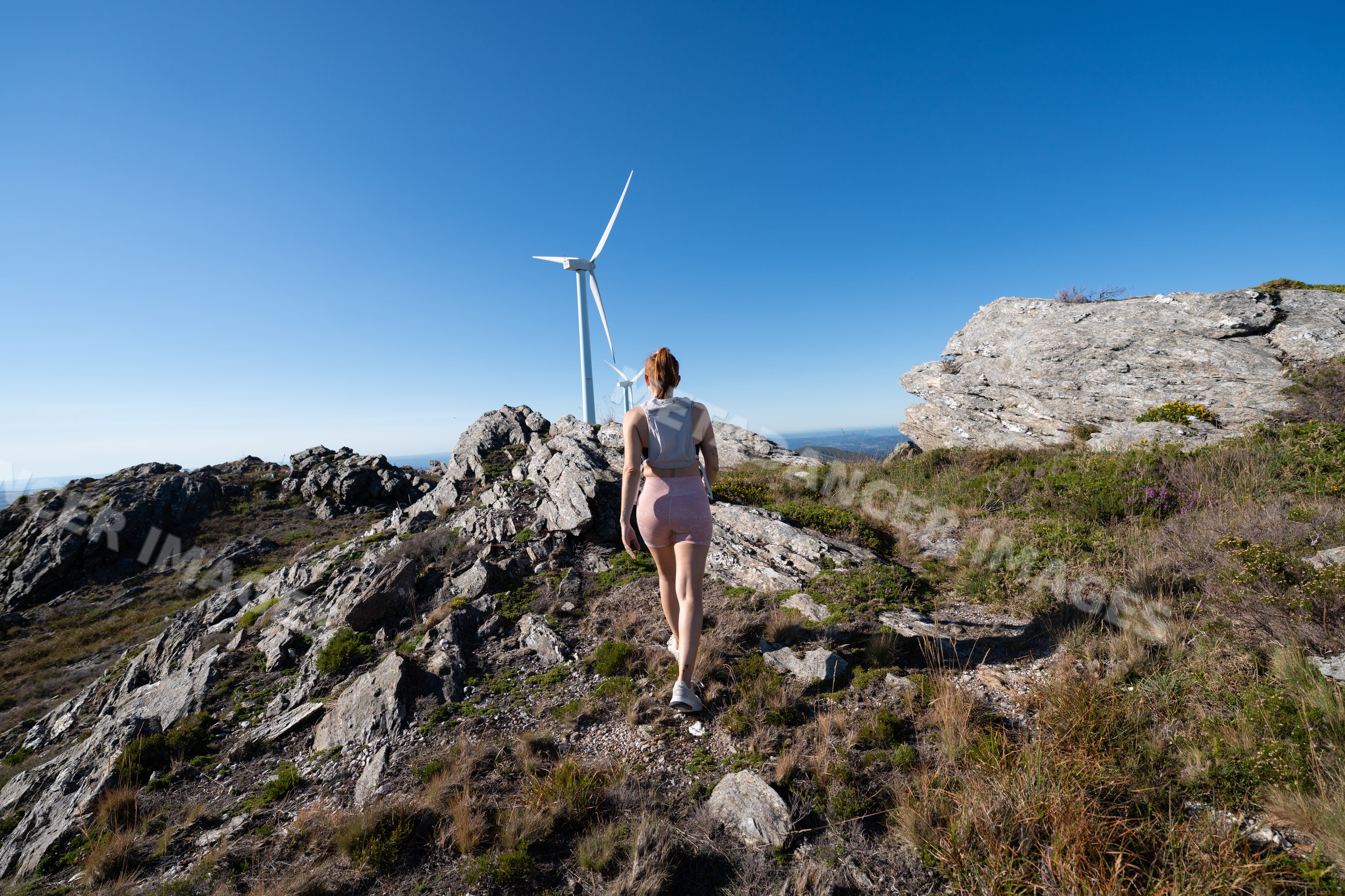 A white woman hiking near wind turbines on a rocky mountain in Galicia