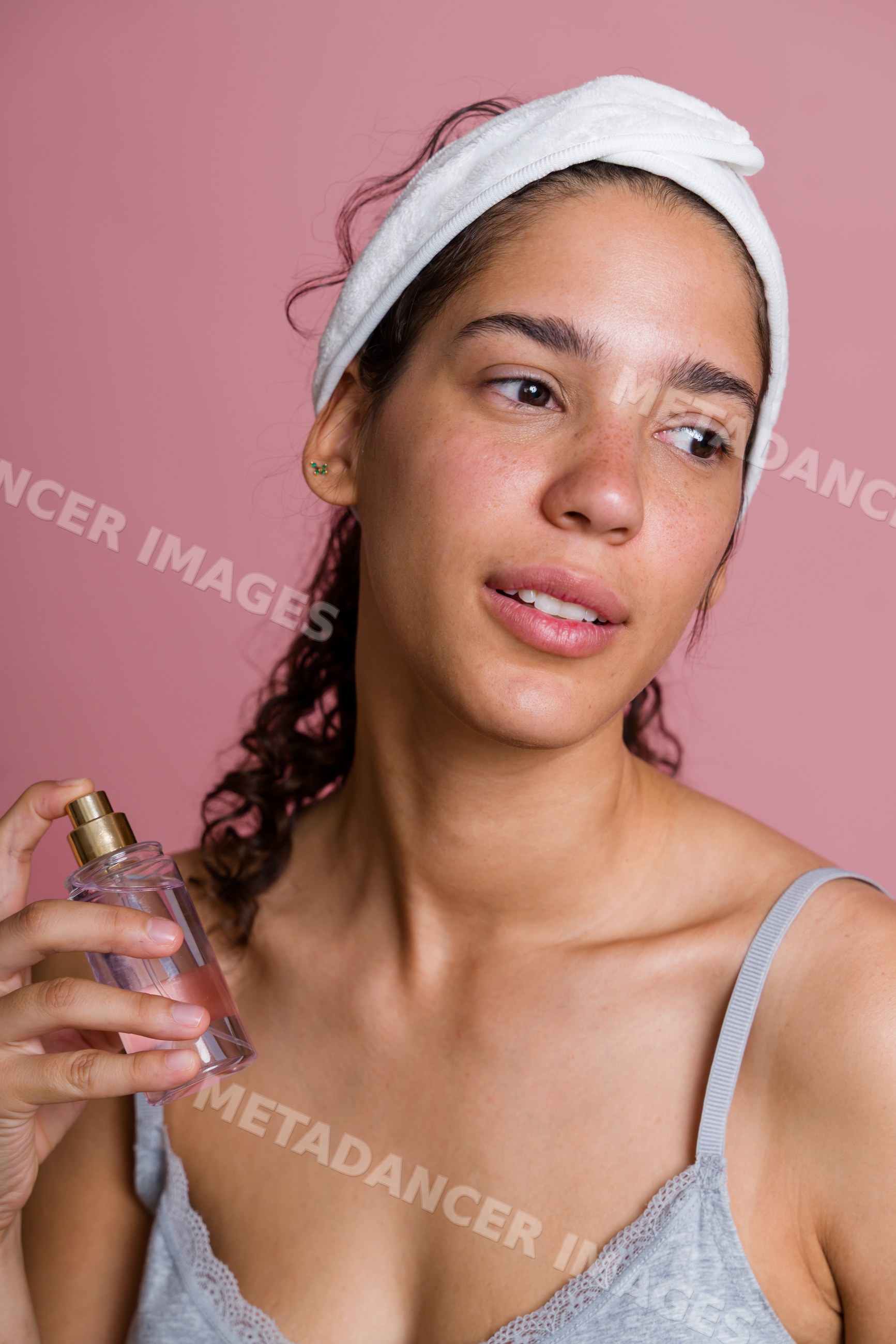 Hispanic woman applying facial spray serum with headband against pink