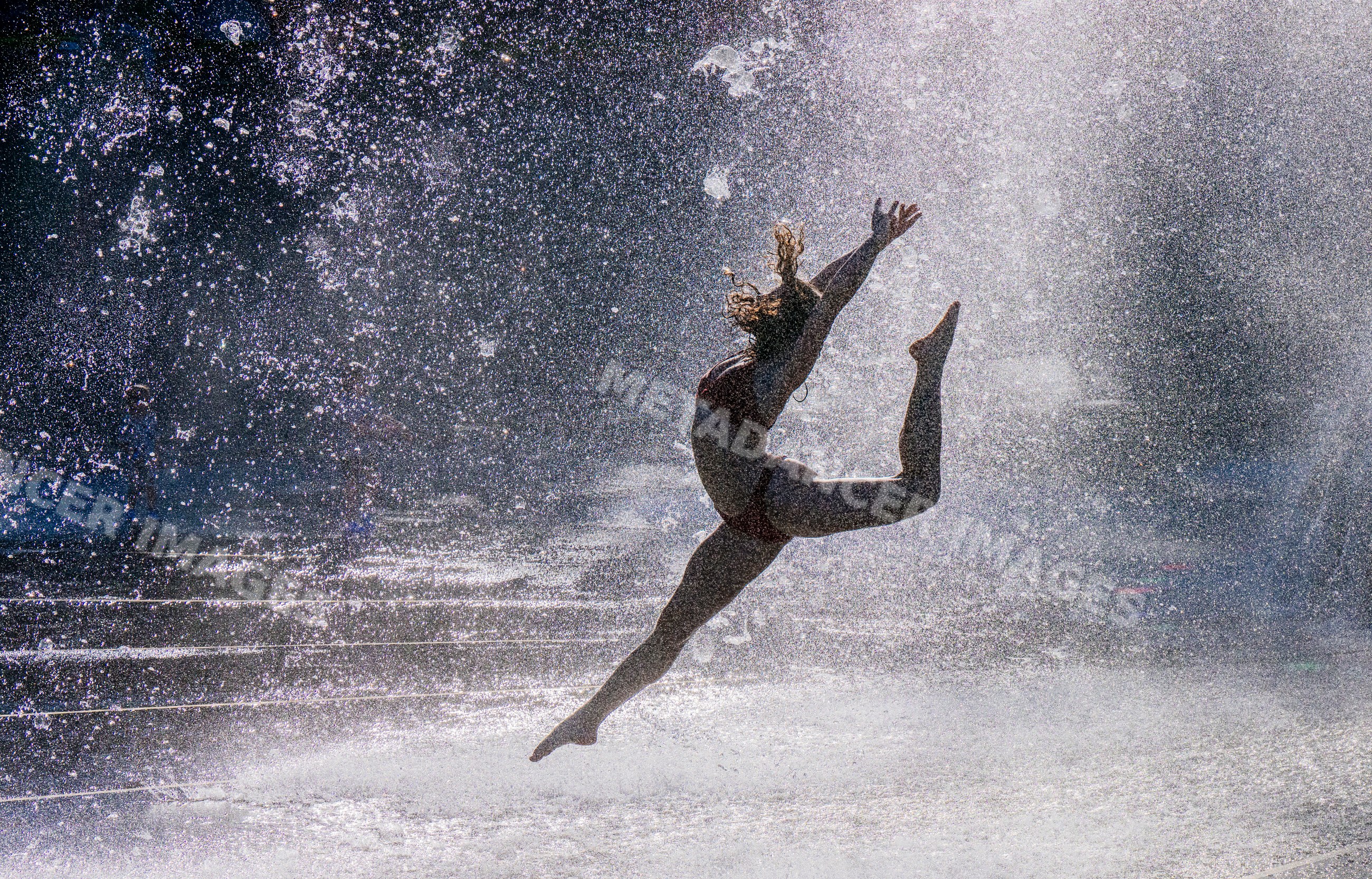 White woman jumping dynamically through outdoor water fountain spray
