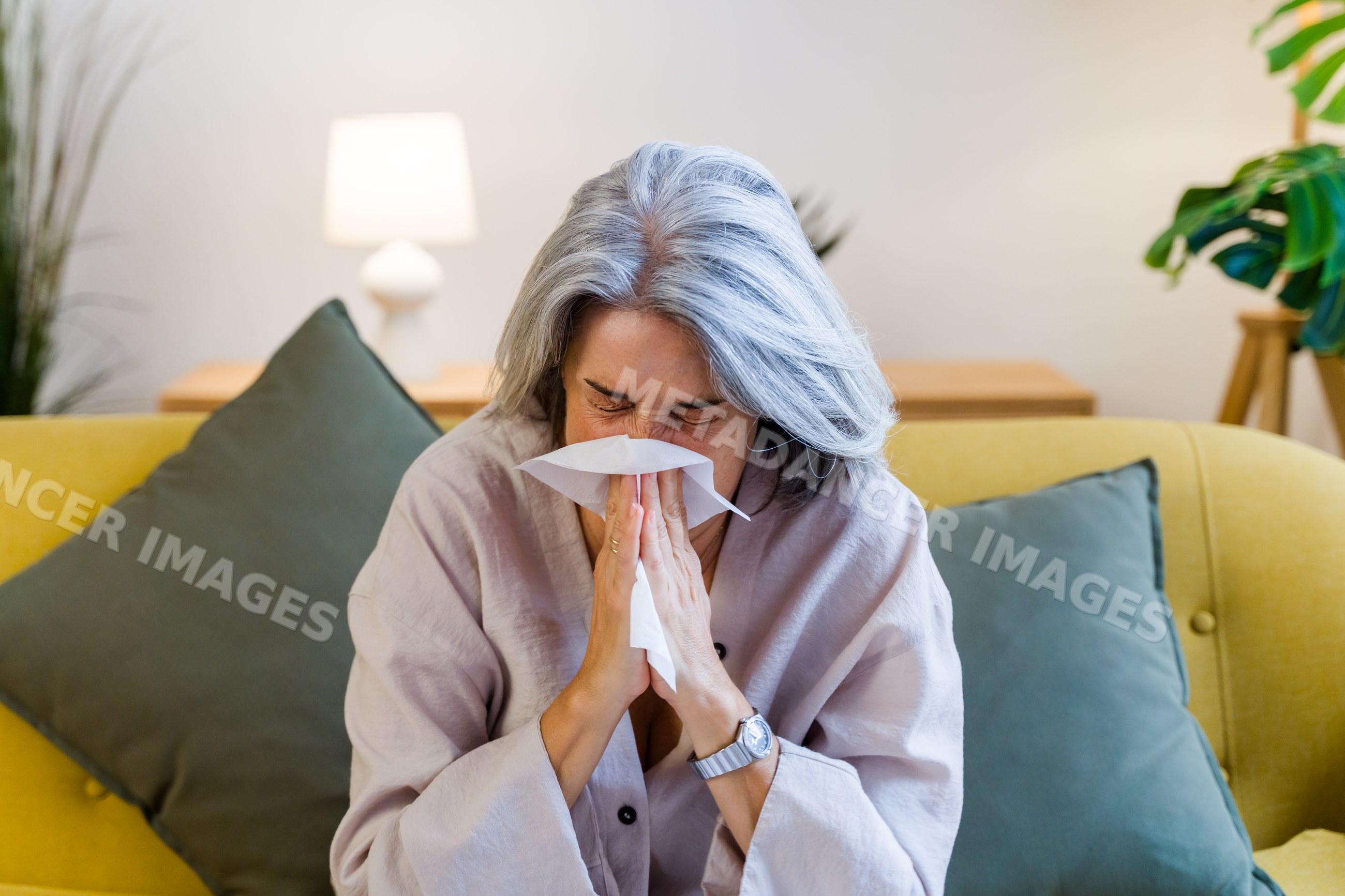 White woman sneezing into tissue on couch in living room
