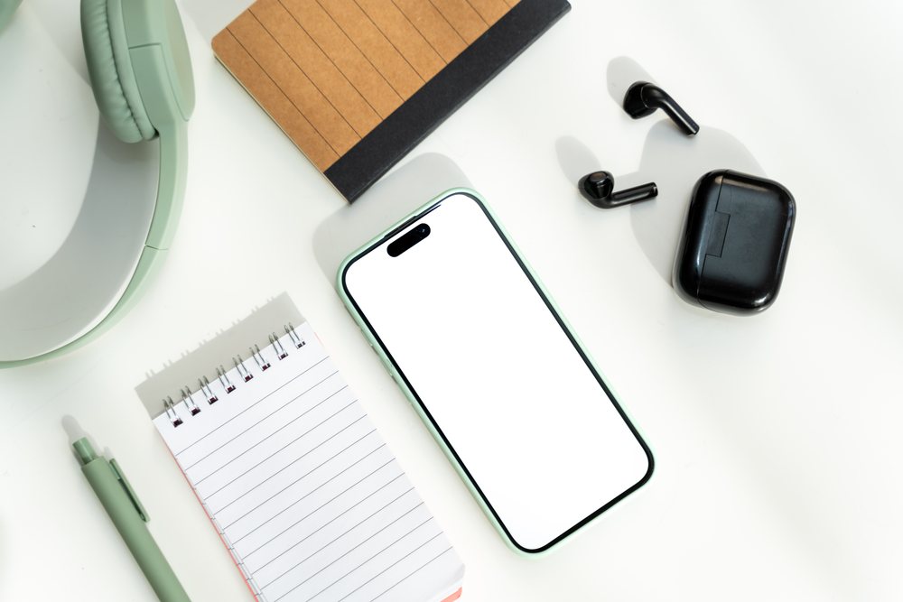 Smartphone with wireless earbuds and office supplies on white desk
