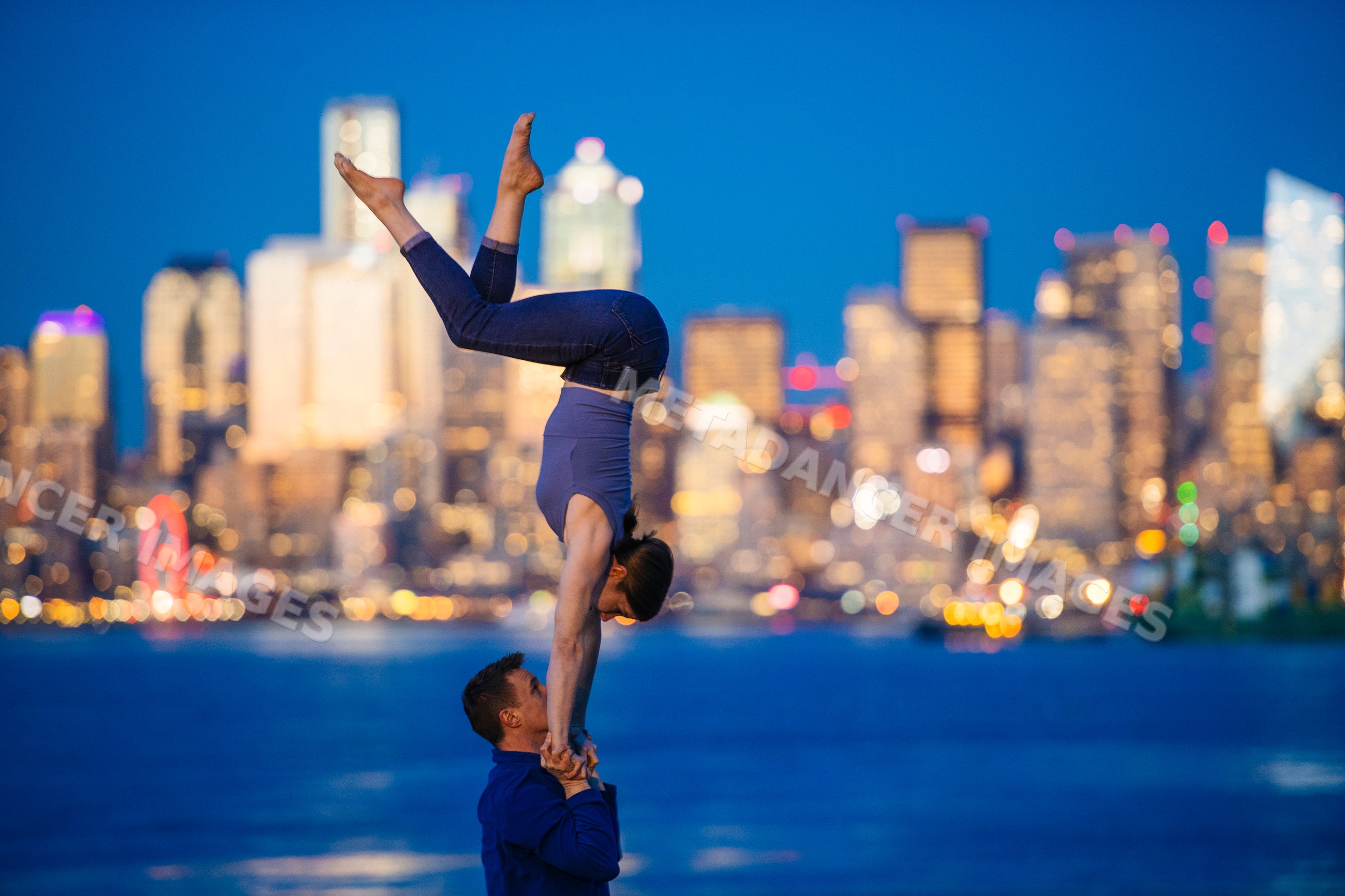Partner acrobatics yoga pose at Seattle waterfront with city skyline