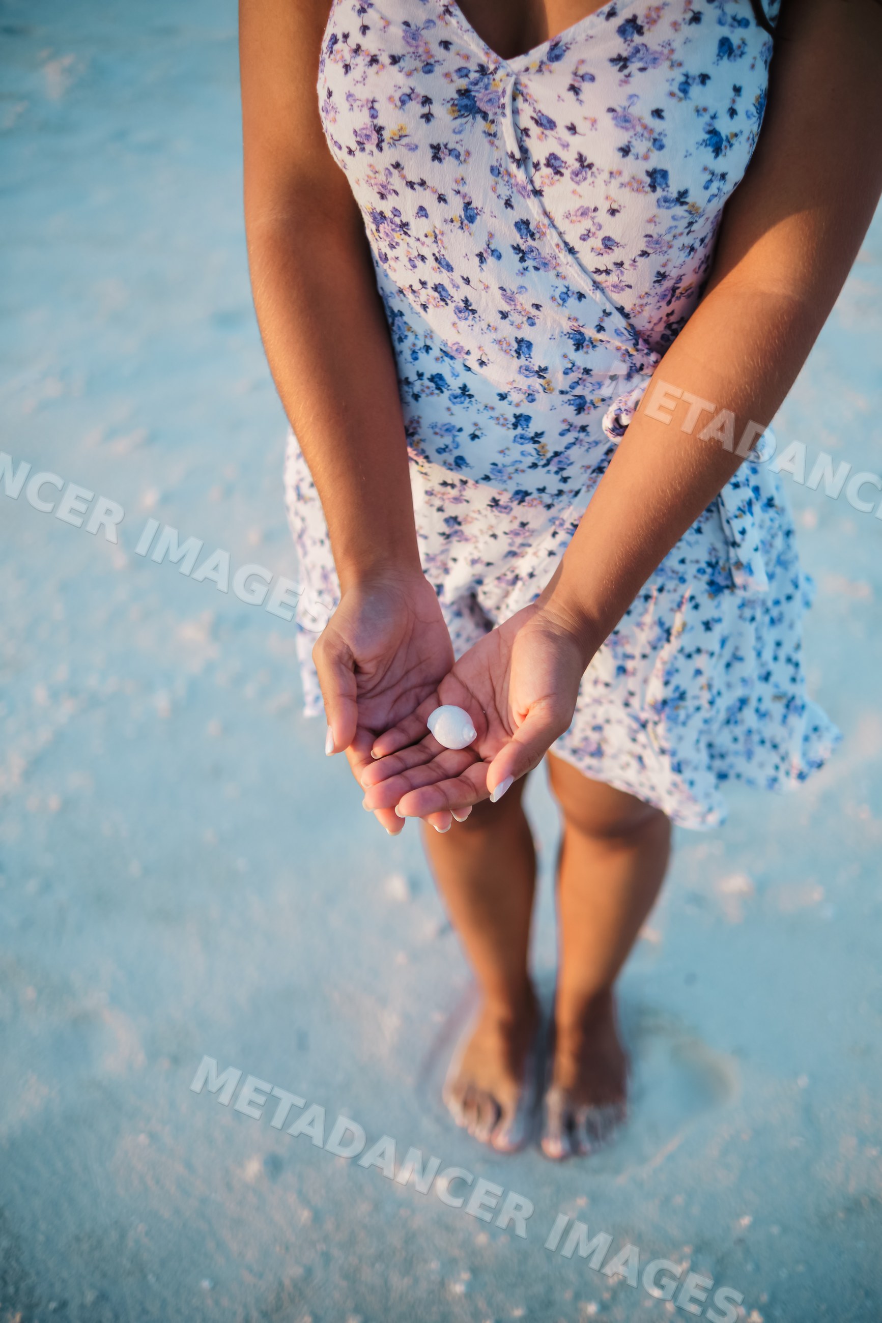 A white woman holding a shell on a sandy beach in a beach
