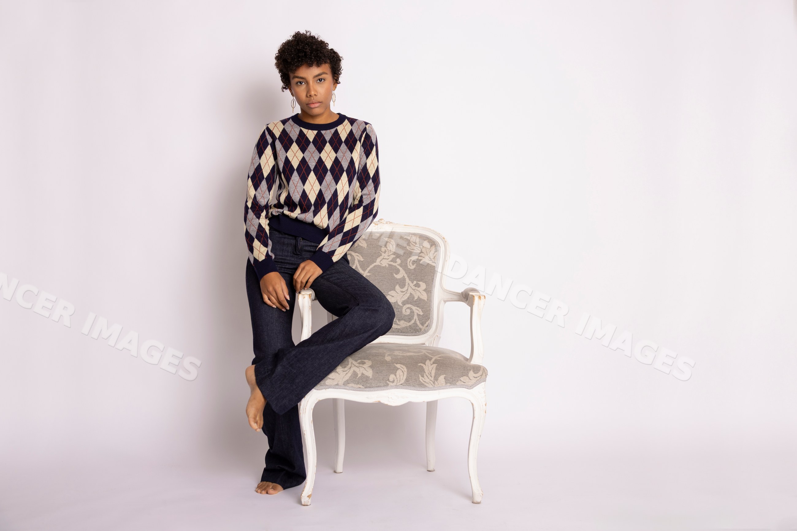Young Hispanic woman posing in argyle sweater and jeans with chair