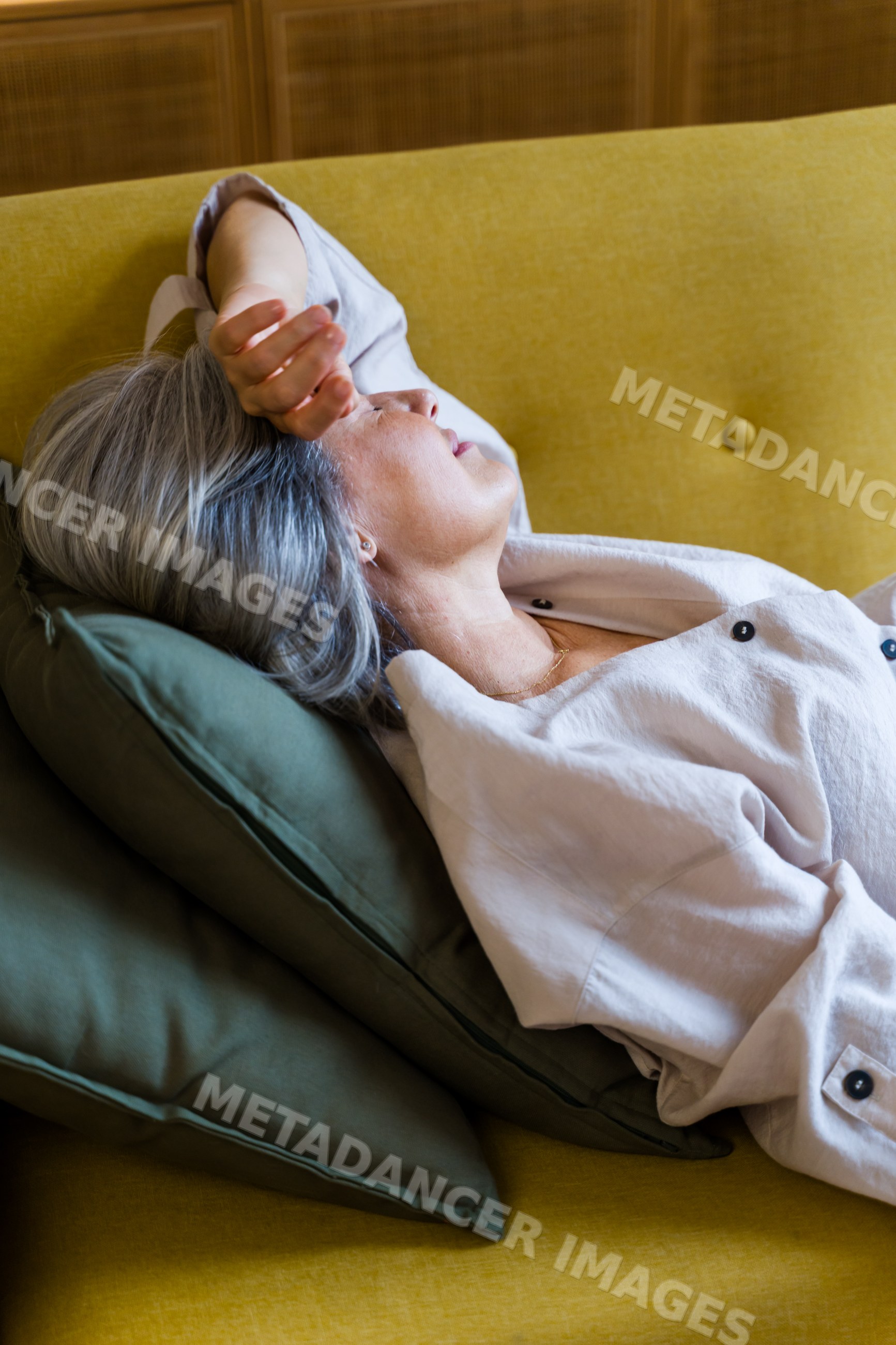 White woman relaxing on yellow sofa with green cushions indoors
