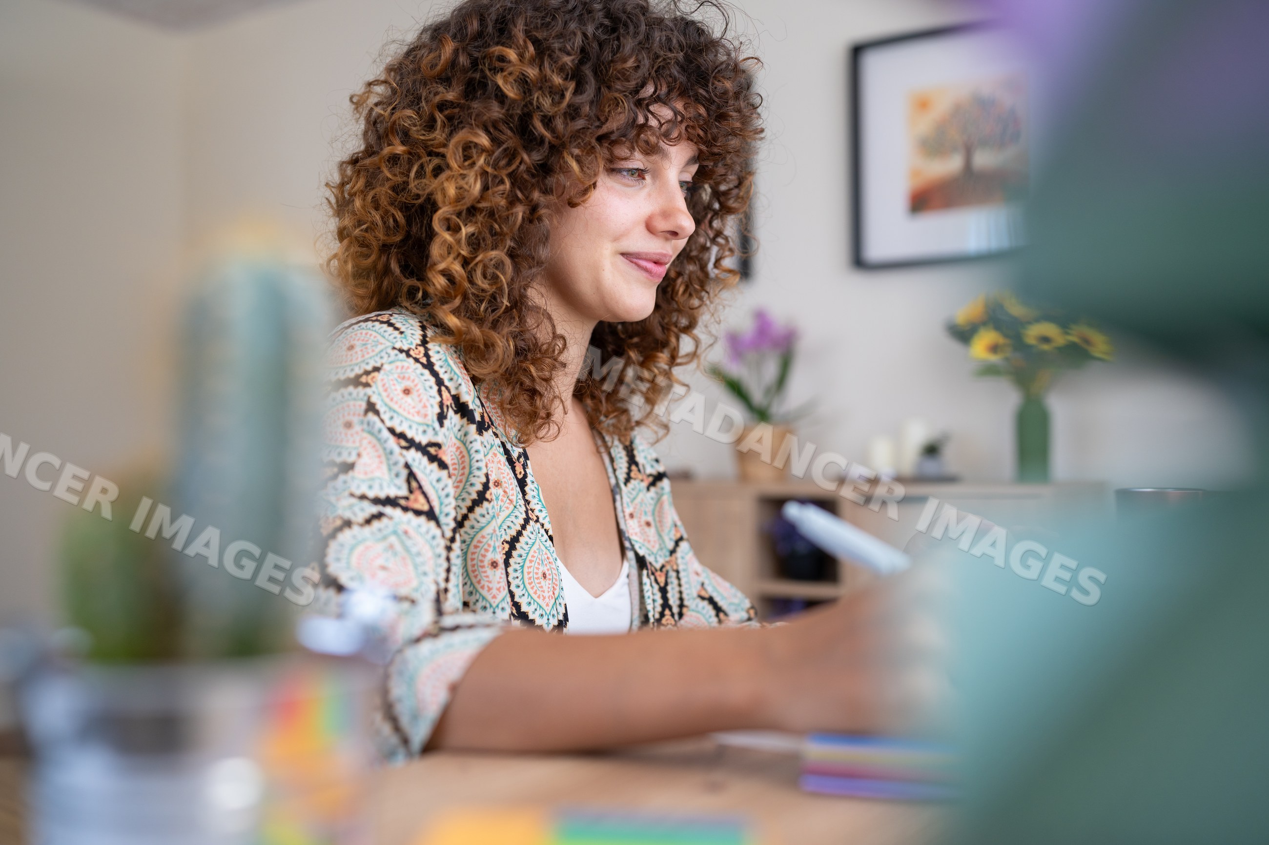 White woman with curly hair writing at a desk in home setting