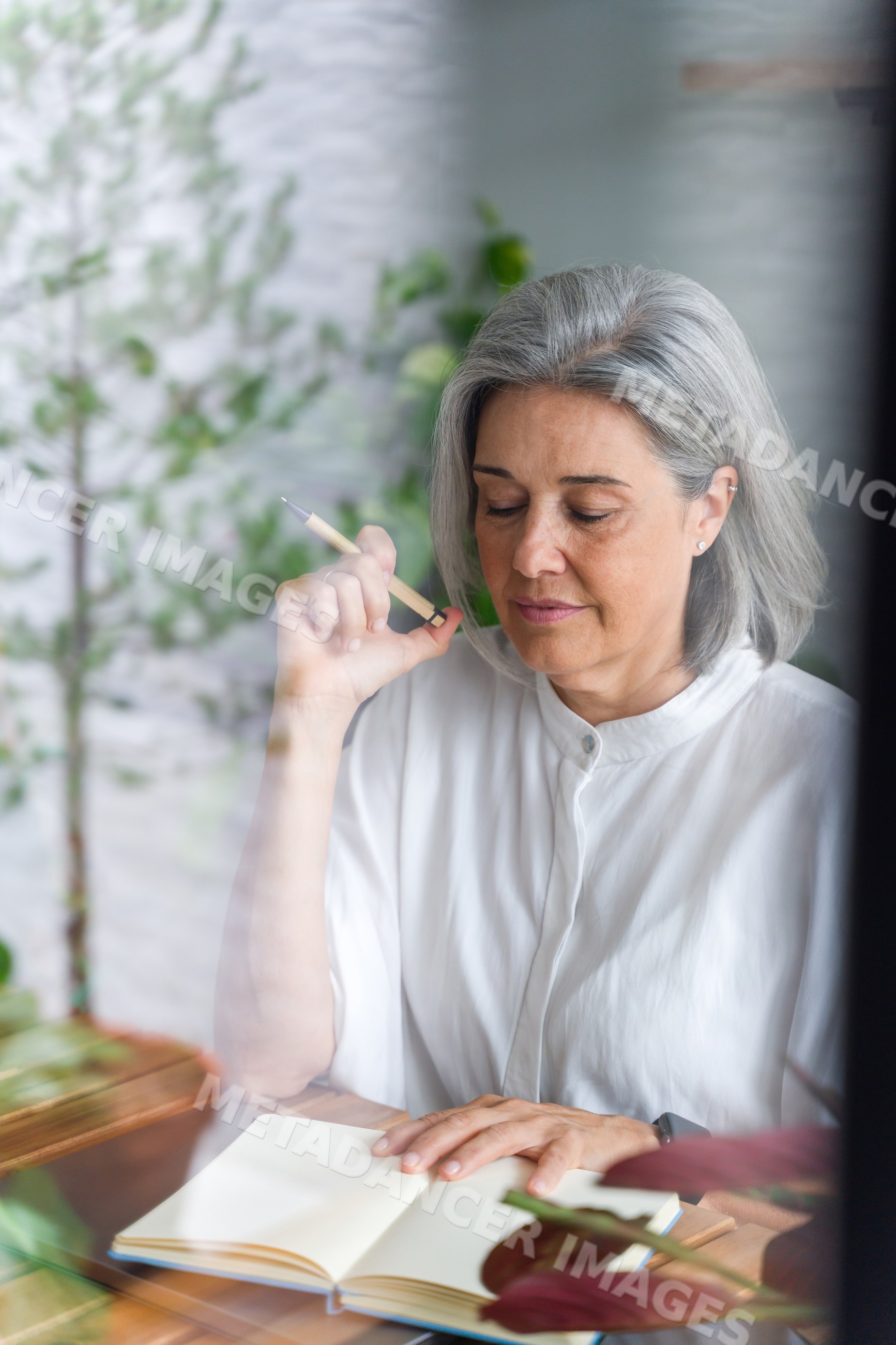 White Woman with grey hair writing in notebook indoors with plants