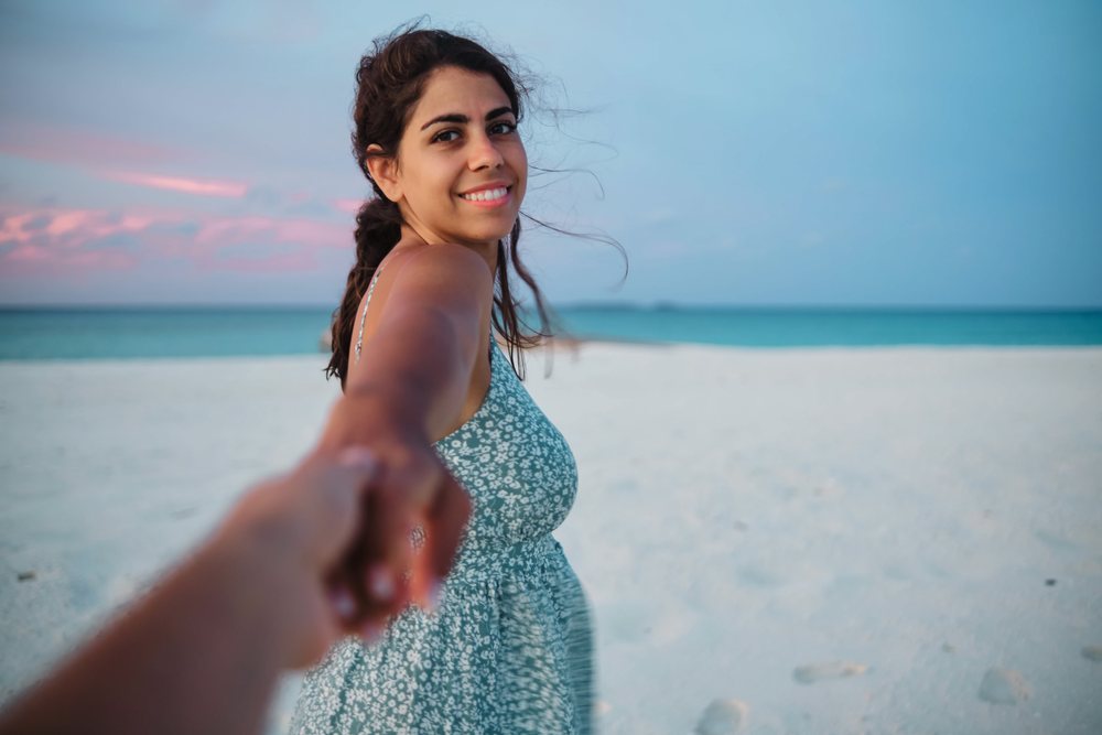 A white woman smiles holding hands with someone on a Maldives beach
