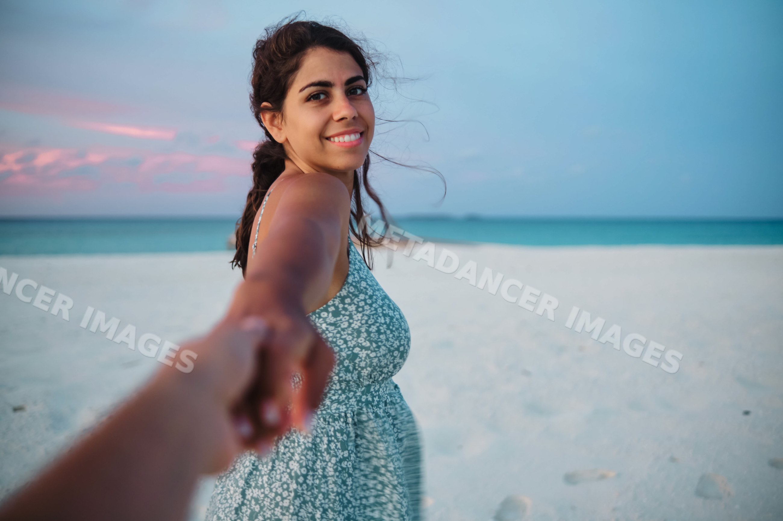 A white woman smiles holding hands with someone on a Maldives beach