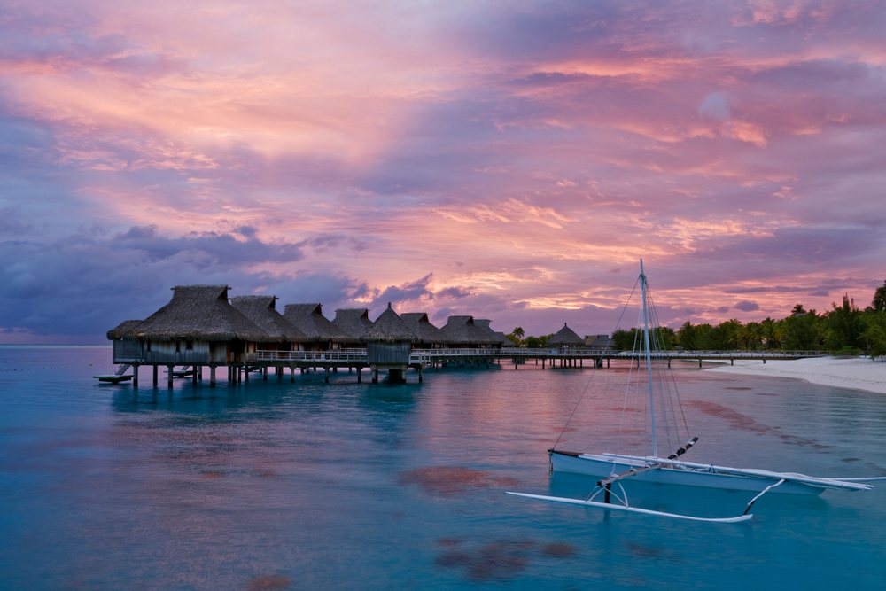 Overwater bungalows and sailboat at sunset, french polynesia