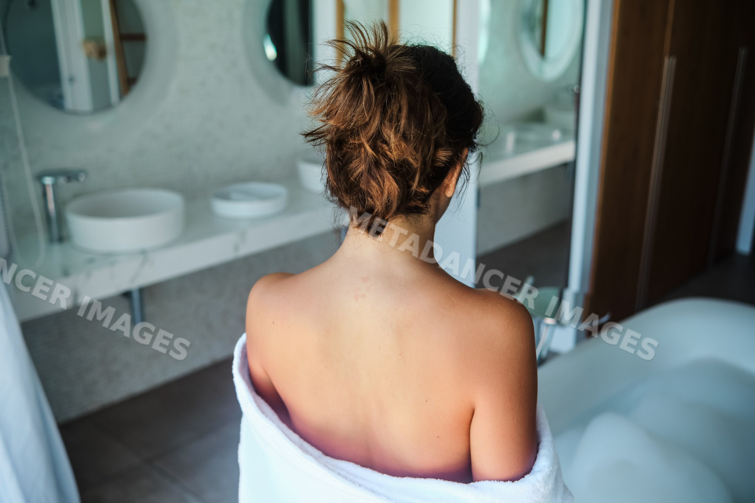 A white woman wrapped in towel relaxing by a foam bathtub