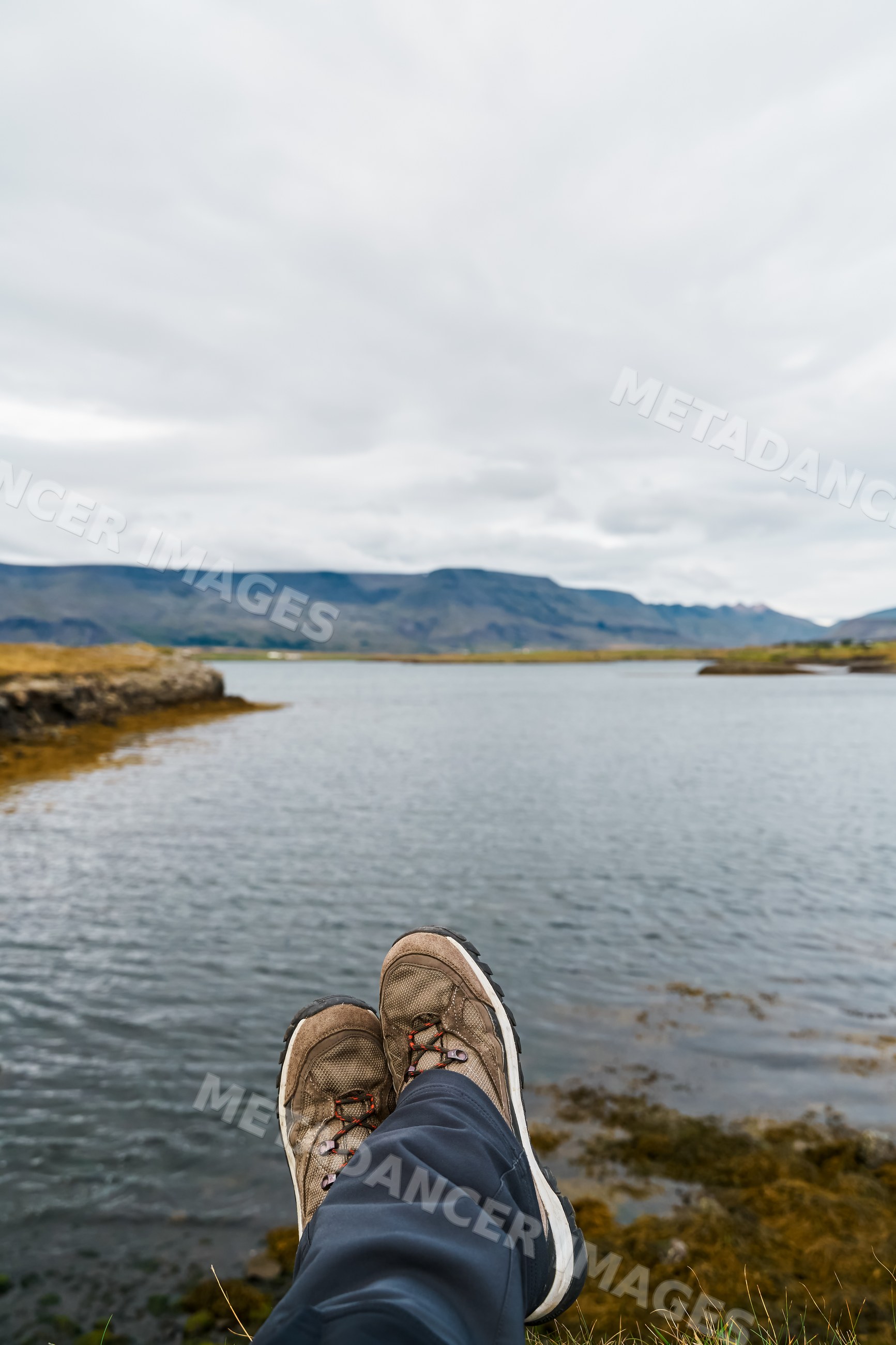 Person relaxing by a lake with hiking boots