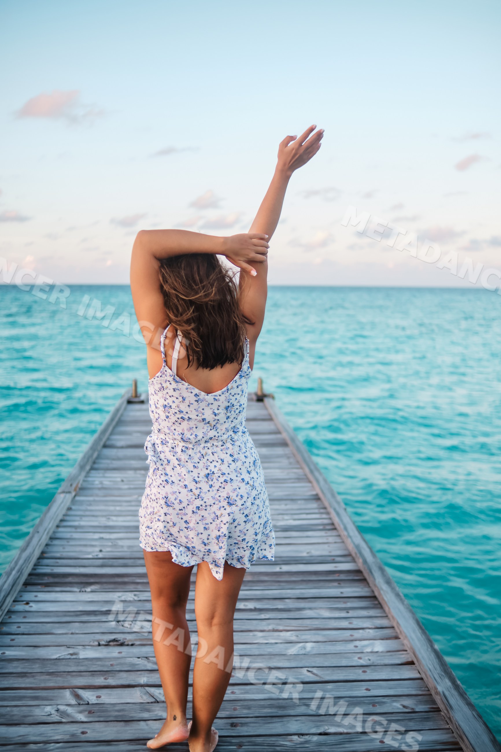 A white woman stands barefoot on a wooden pier overlooking the ocean